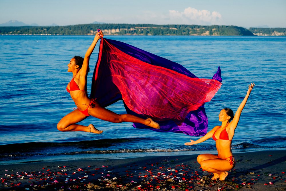 Two women performing yoga partner acrobatics on a beach with ocean