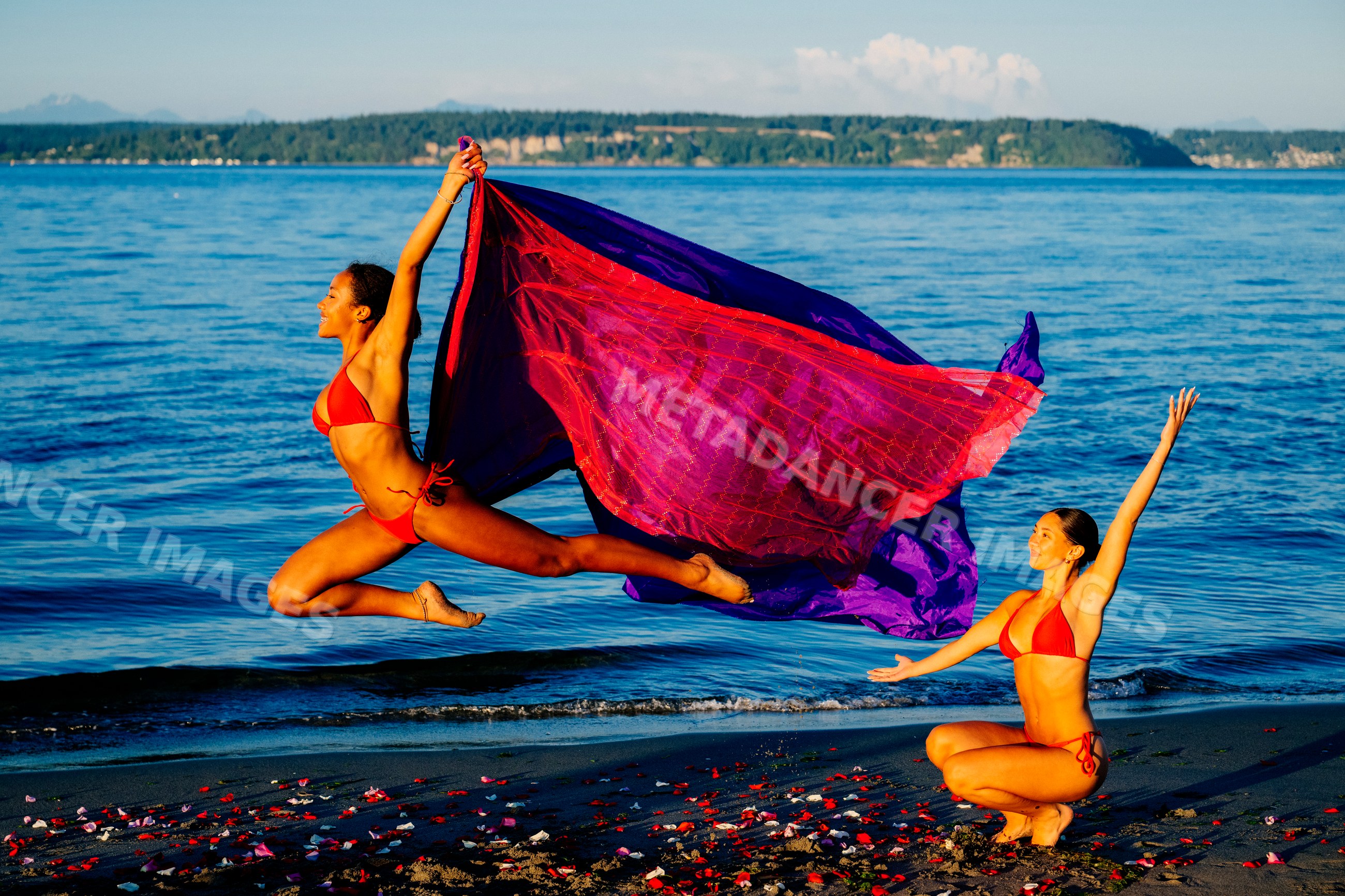 Two women performing yoga partner acrobatics on a beach with ocean