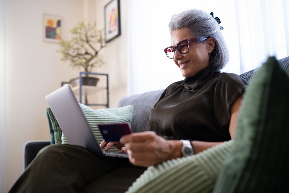 White woman using laptop and holding credit card on couch