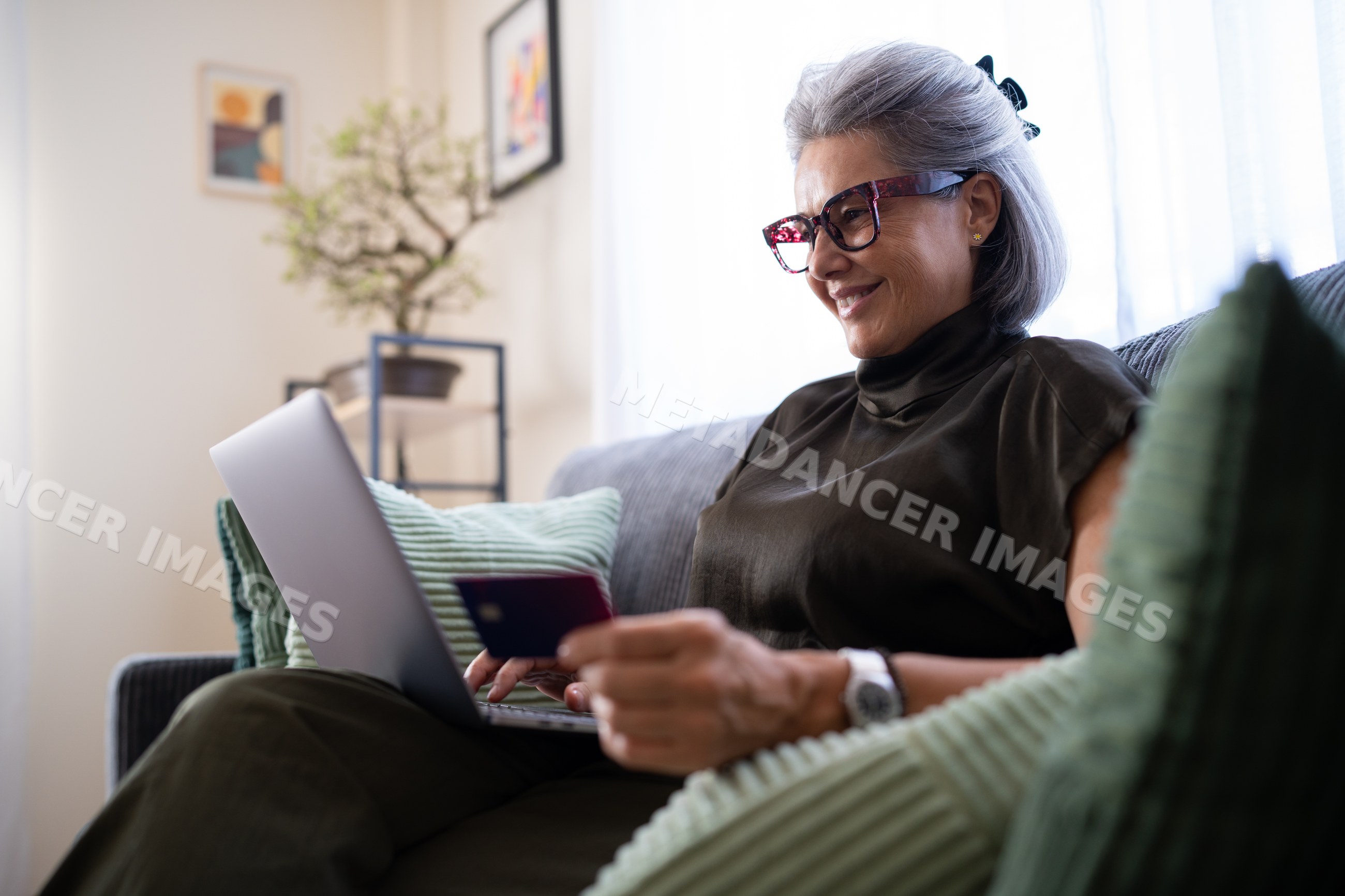 White woman using laptop and holding credit card on couch
