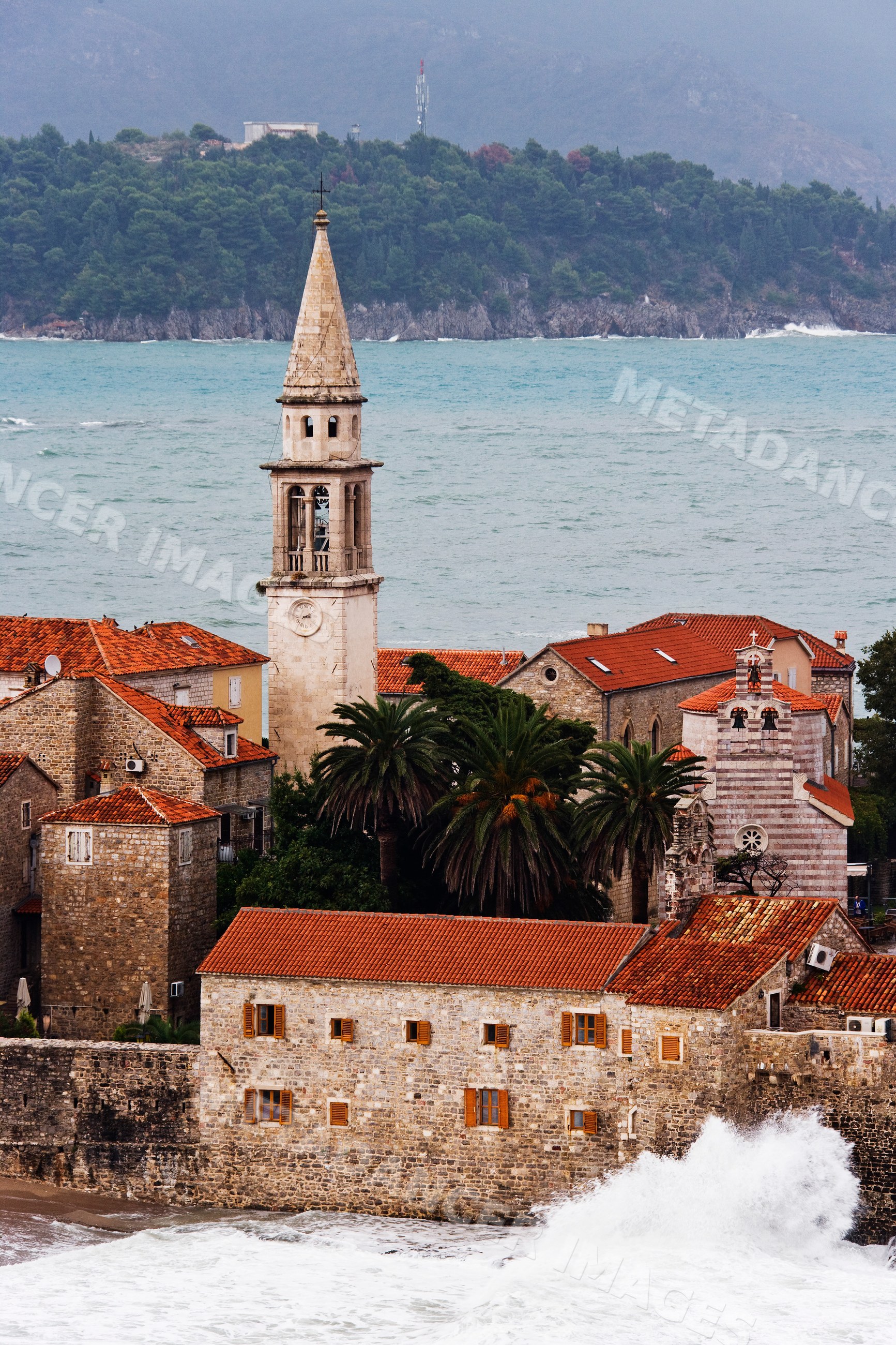 Budva coastal town with church tower and waves on mediterranean sea