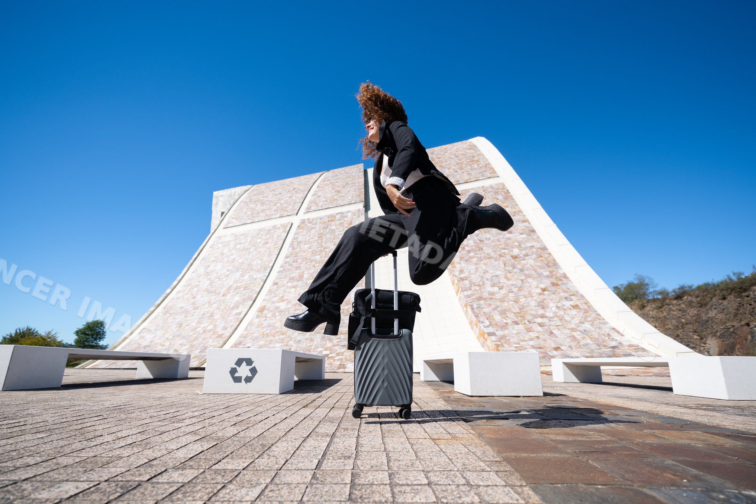 Businesswoman jumping with suitcase in urban plaza