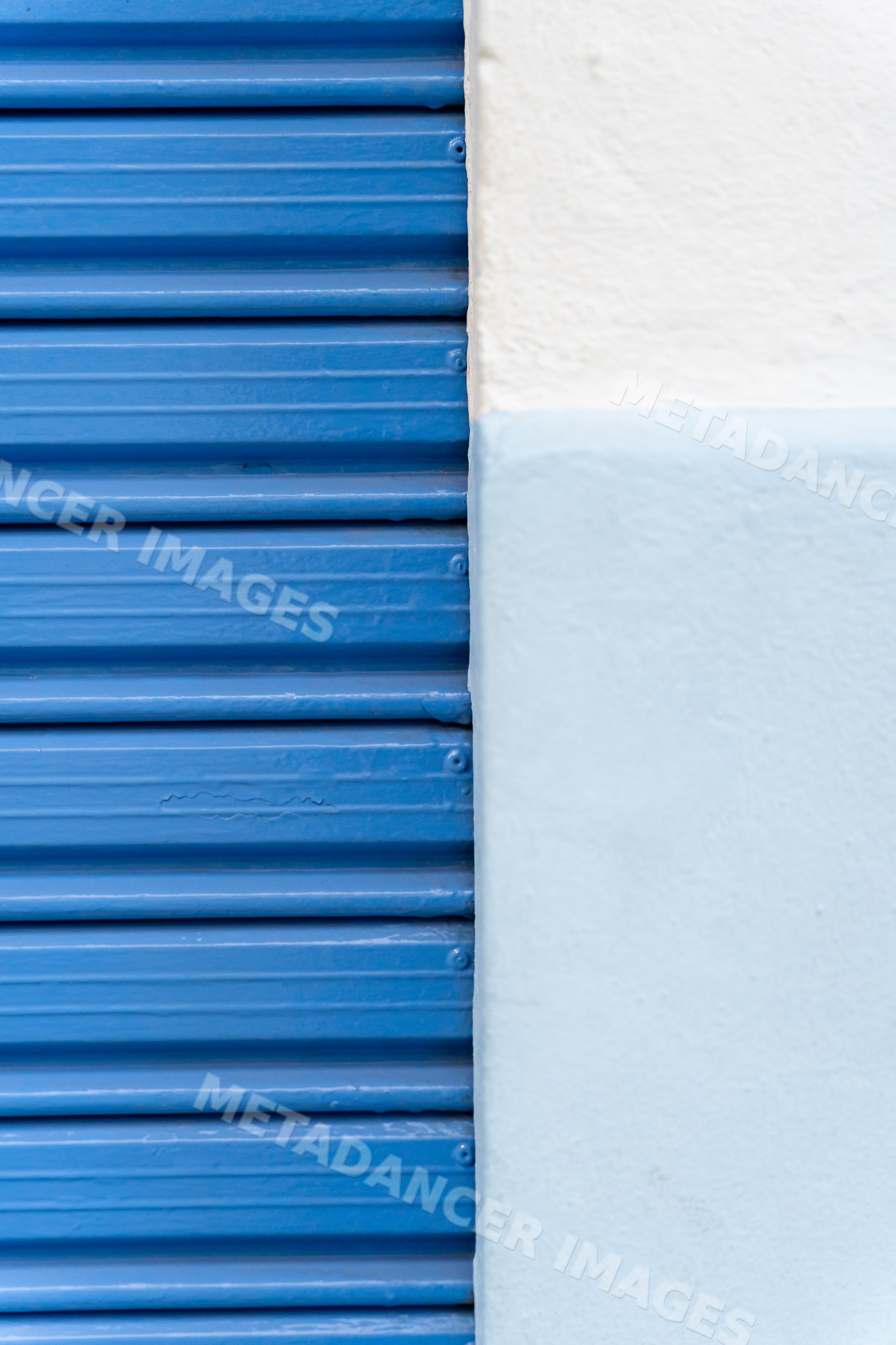 Blue metal shutter beside white painted textured wall
