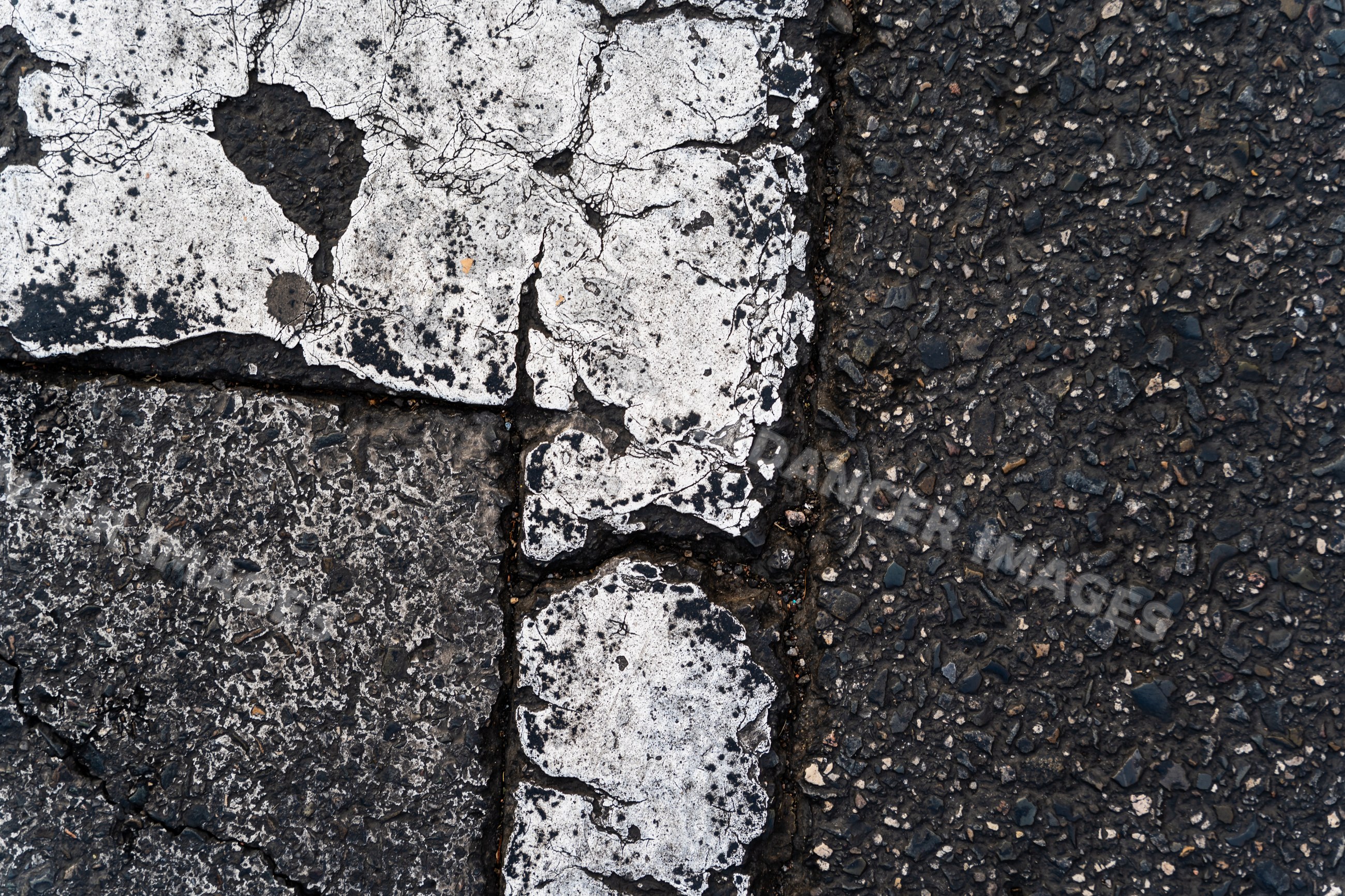 Closeup of worn and cracked white road markings on asphalt surface