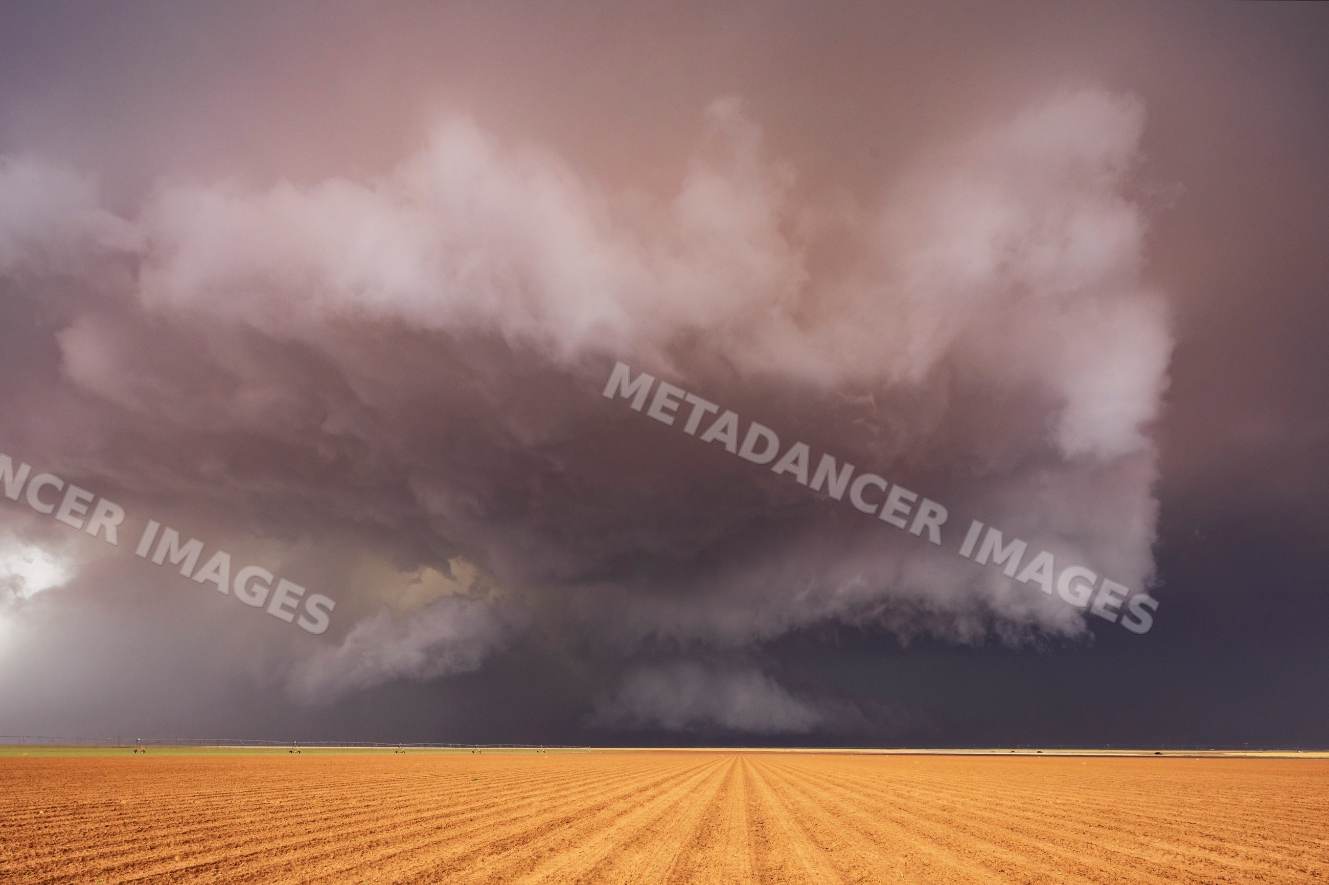 Supercell thunderstorm over a brown plowed field in Morton, texas