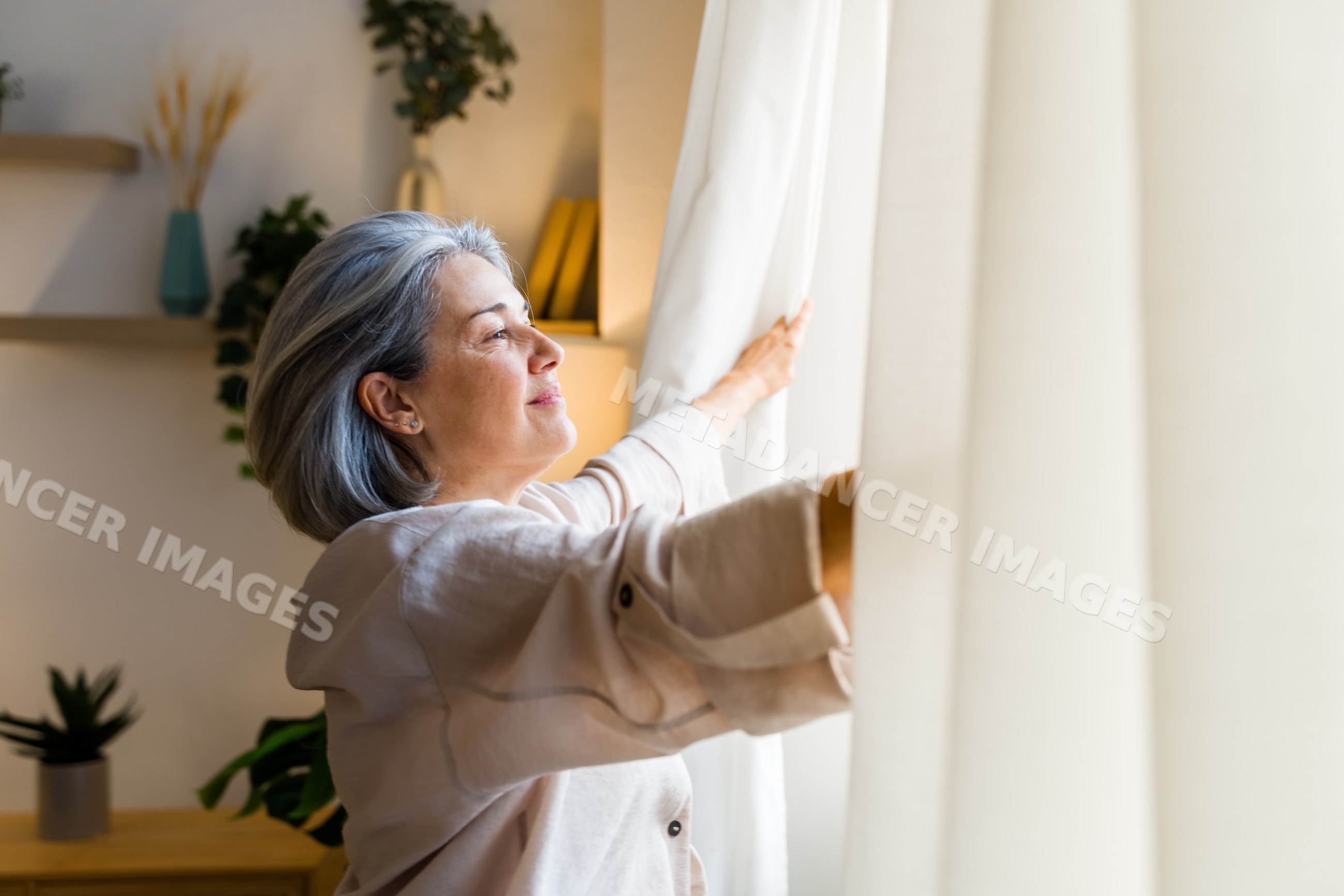 White woman opening curtains to let natural light into cozy home