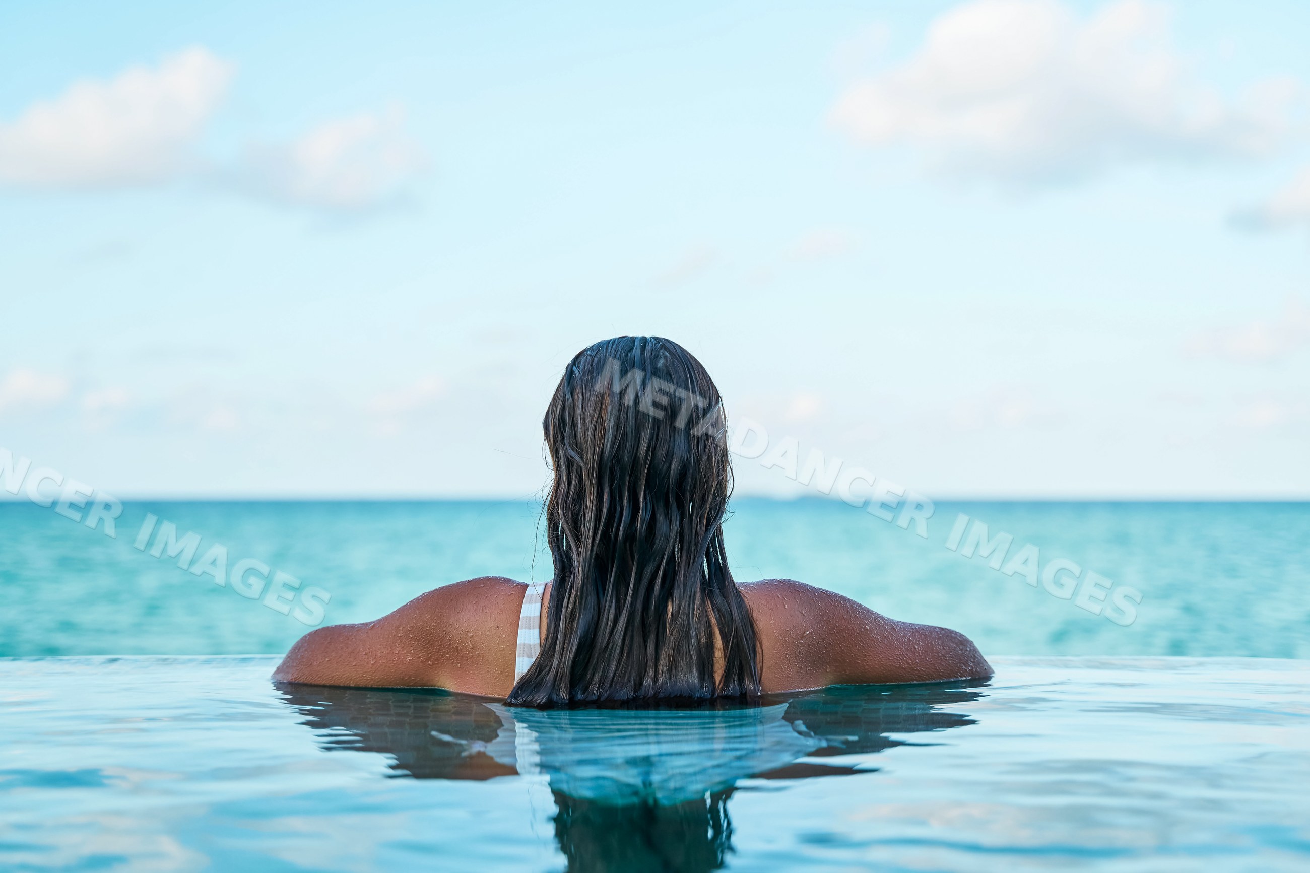 A white woman relaxing in an infinity pool overlooking the ocean