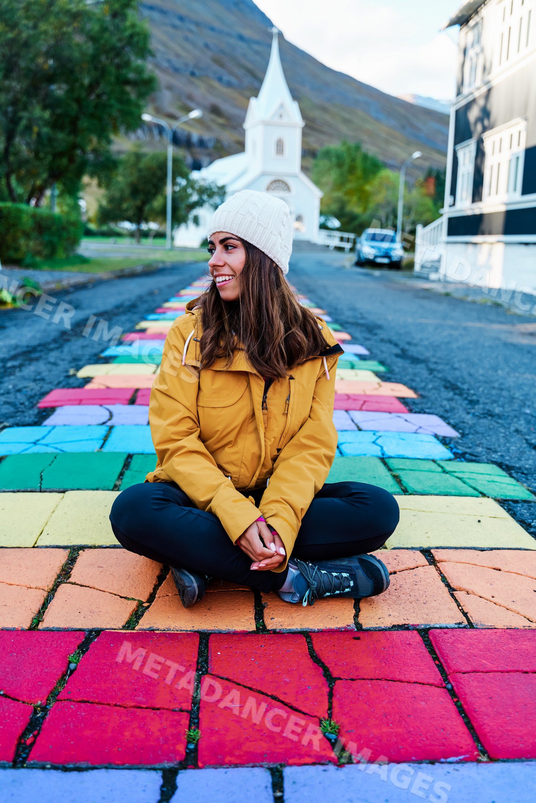 A white woman sits on a rainbow-painted cobblestone street with church