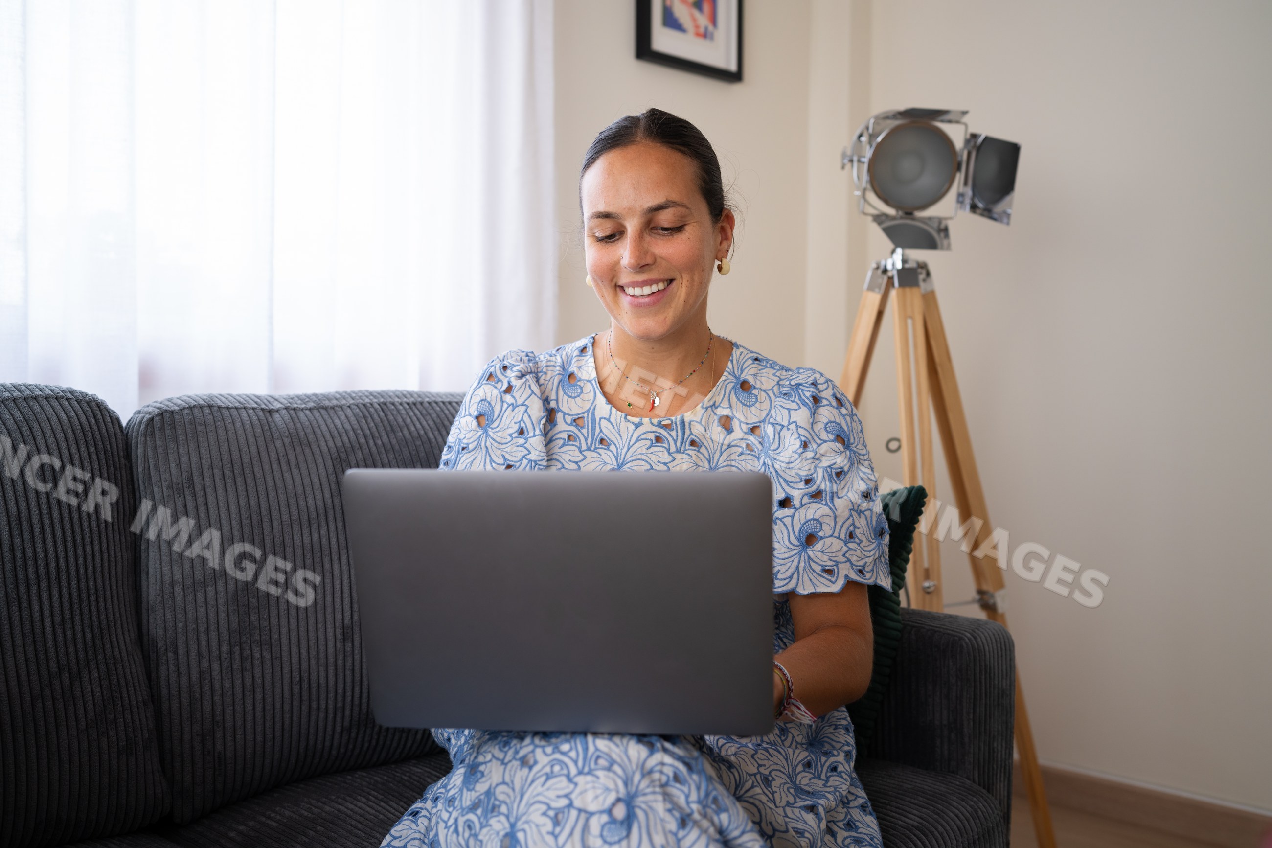 White woman working remotely on laptop seated on sofa with floor lamp