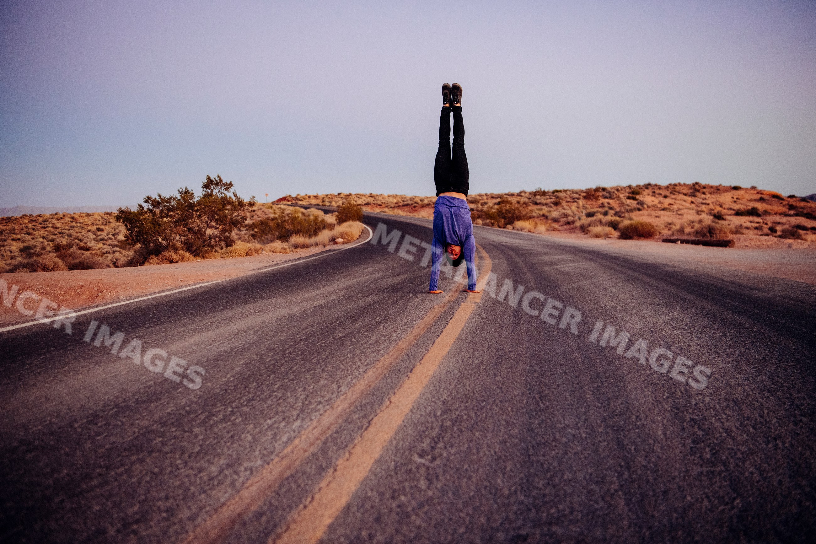 White person doing handstand acrobatics on curved desert road