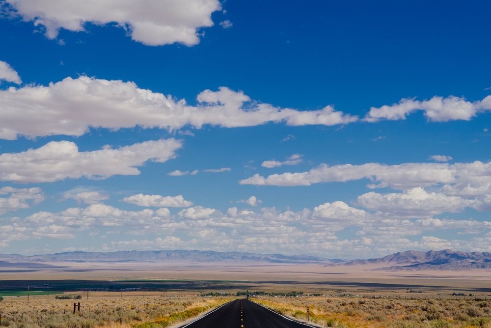Straight empty highway crossing desert landscape under blue sky