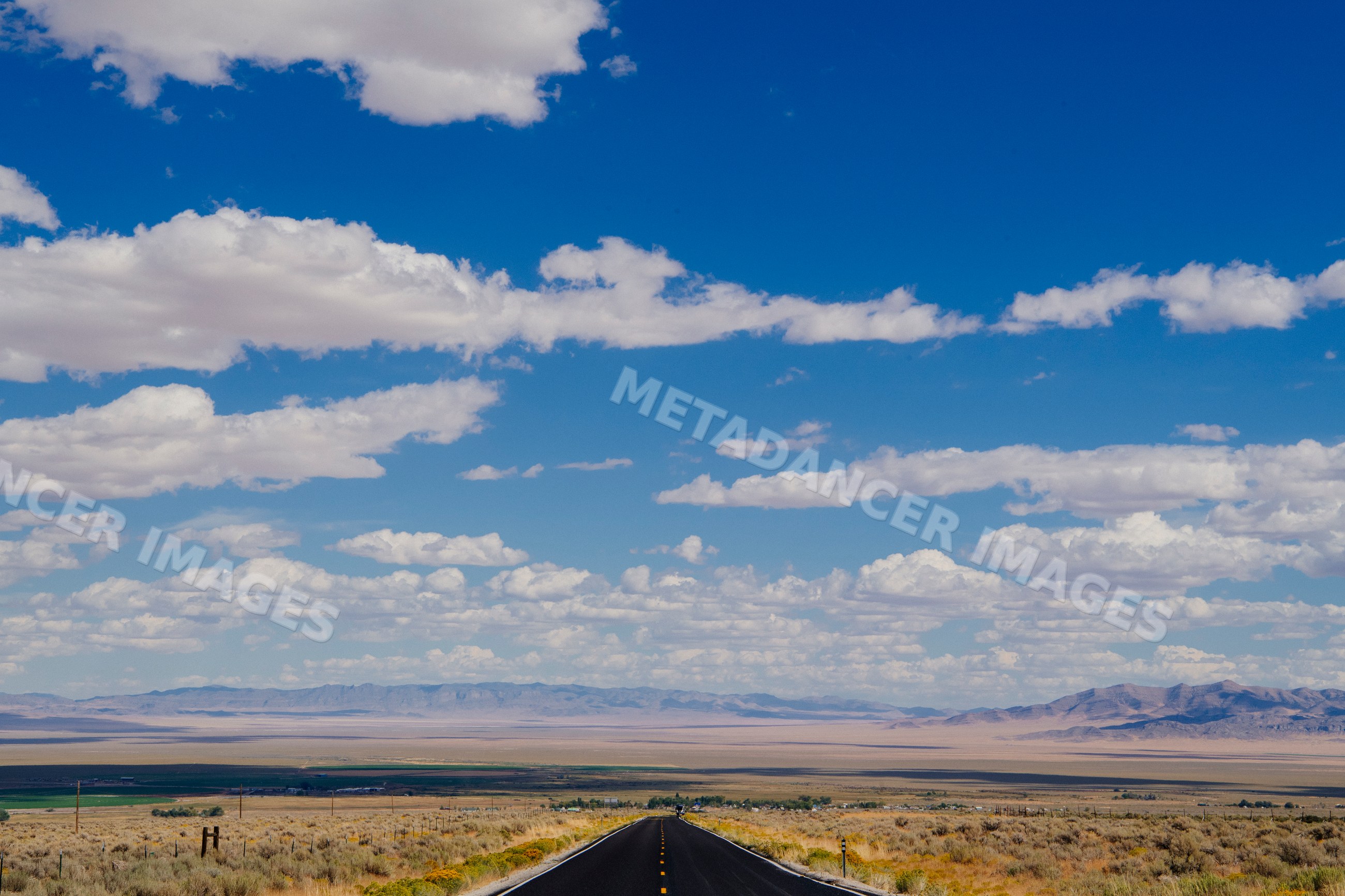 Straight empty highway crossing desert landscape under blue sky