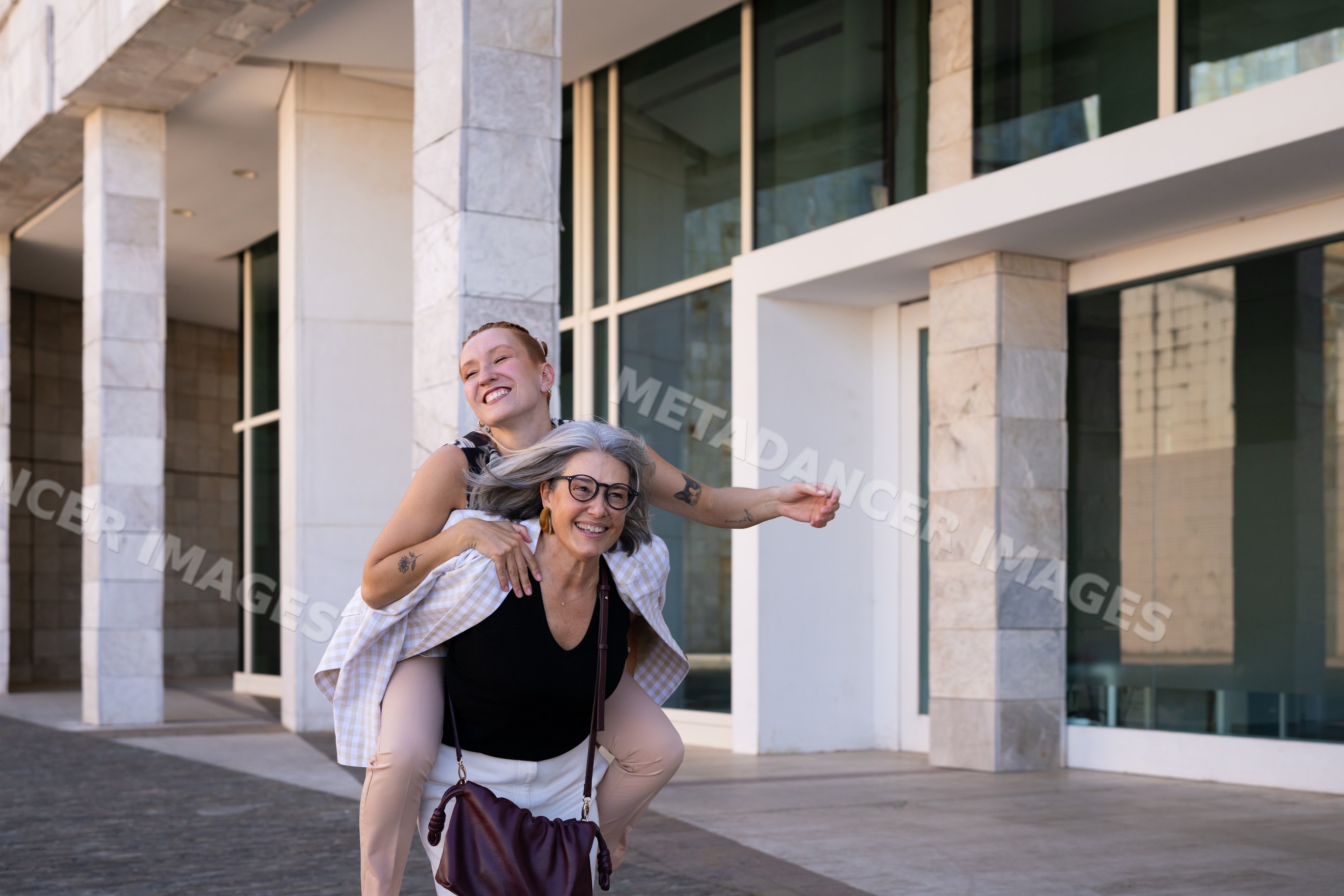 Two white women enjoying a piggyback ride outside modern building