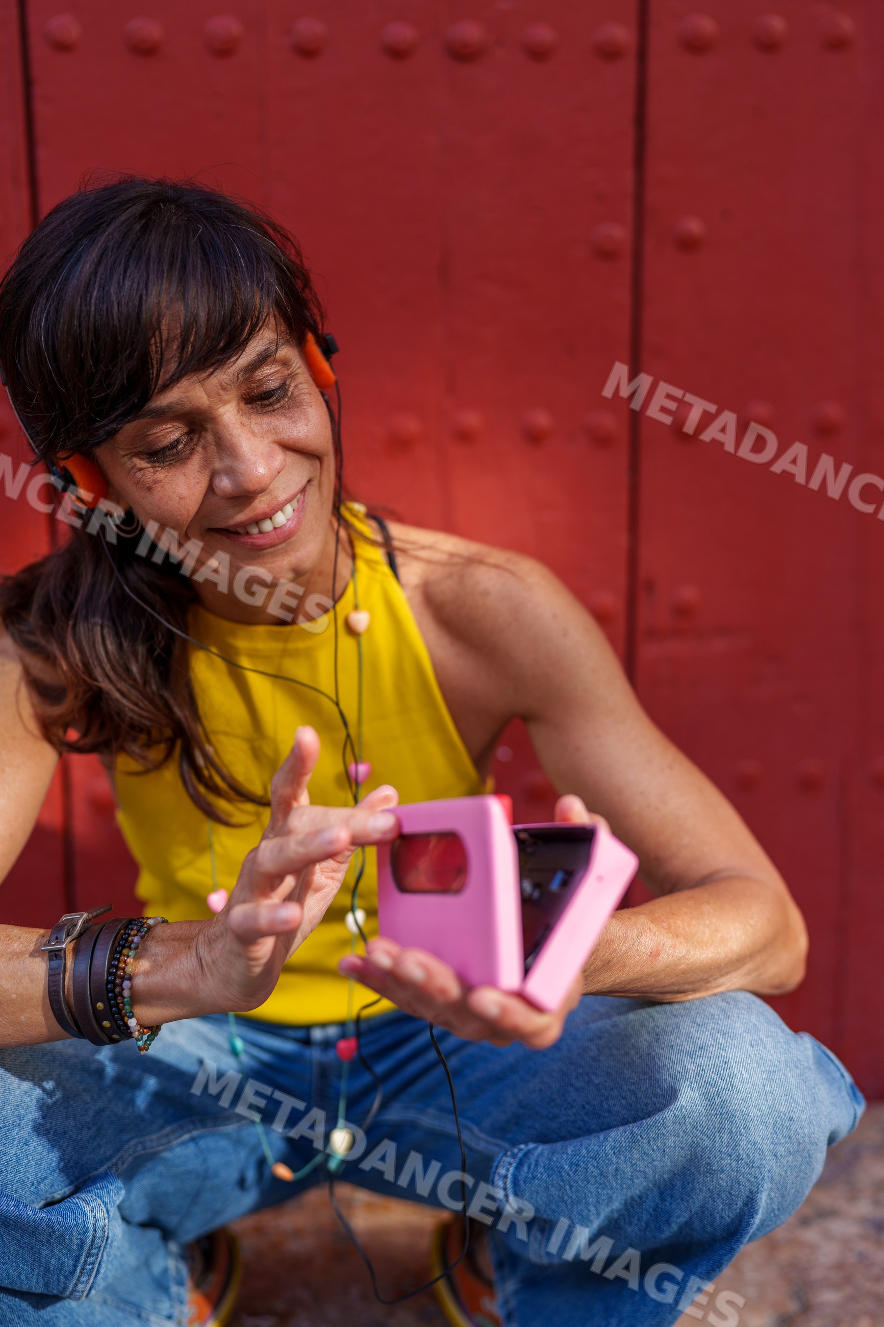 Hispanic woman holding pink instant camera squatting against red wall