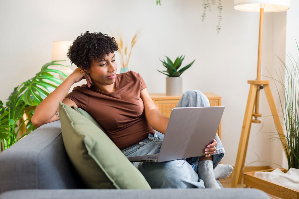 African American woman relaxing on sofa using laptop