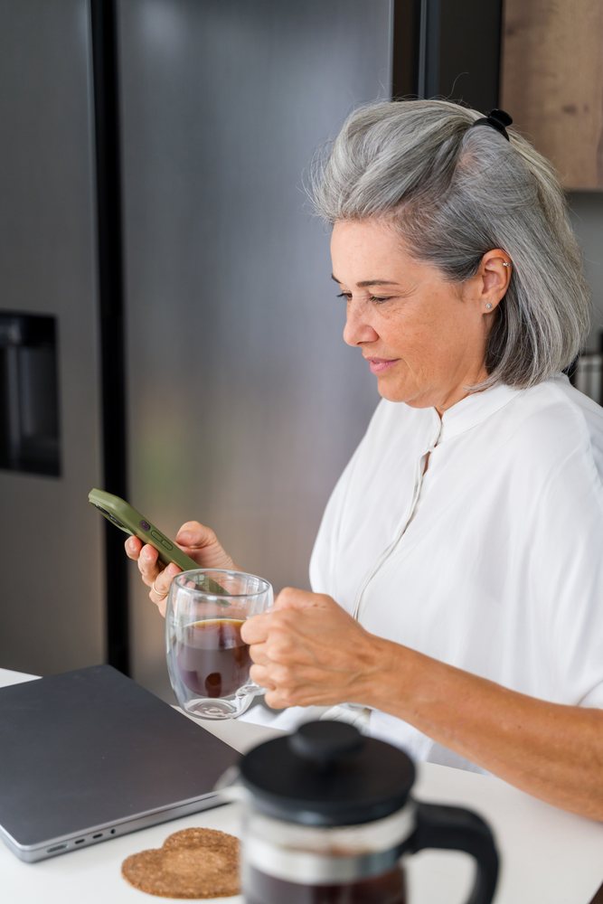 Mature white woman using smartphone and drinking coffee