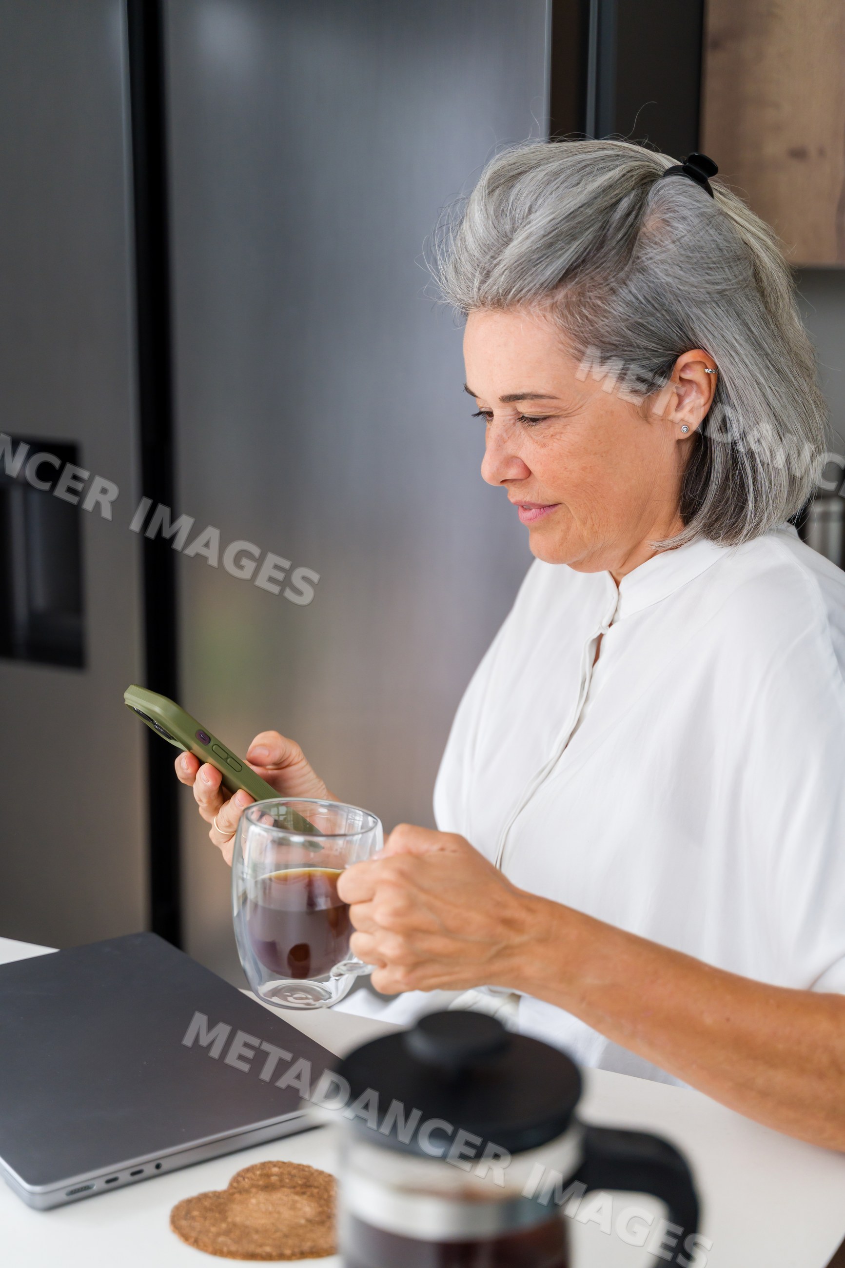 Mature white woman using smartphone and drinking coffee