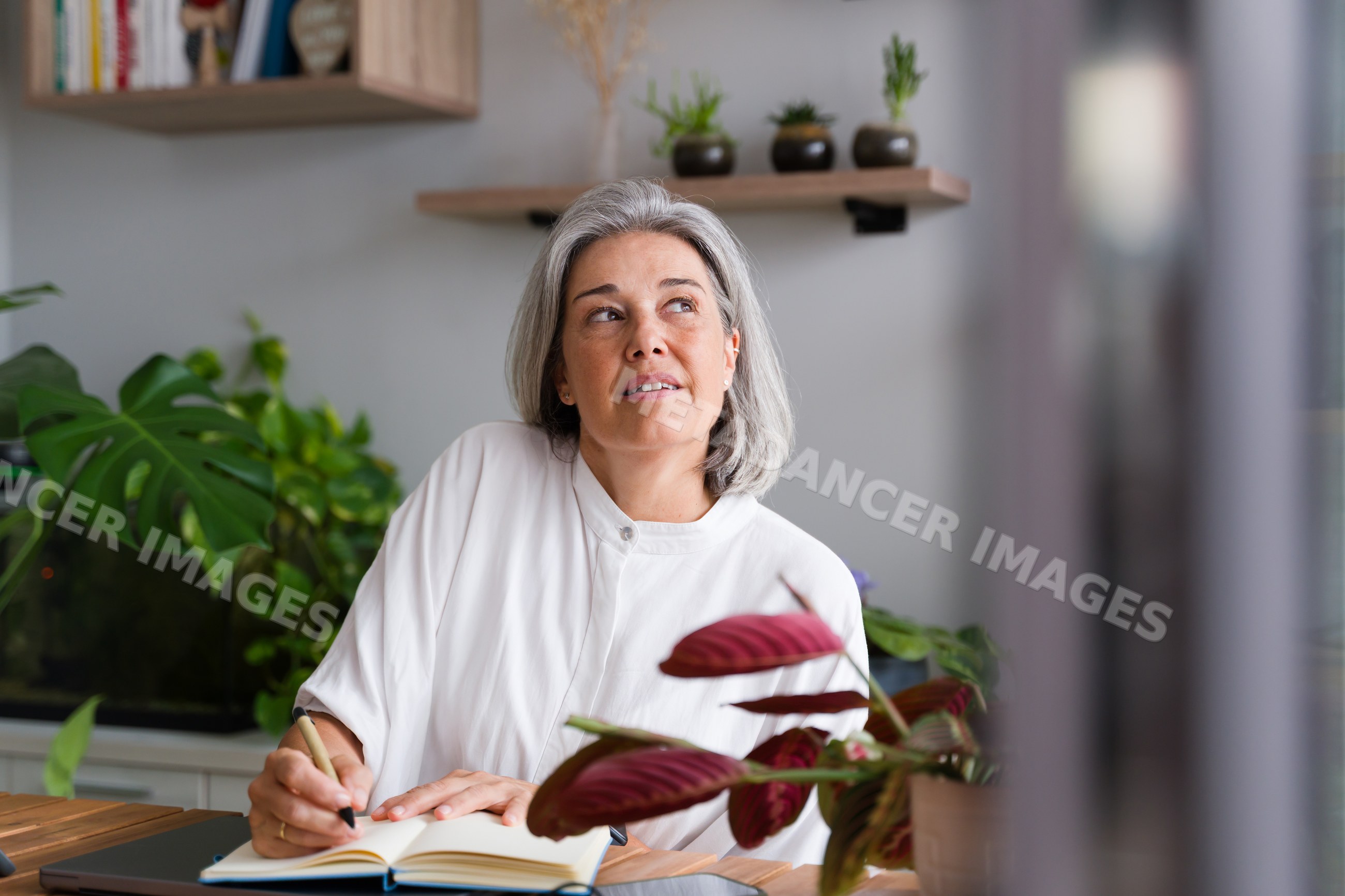 White Woman writing in notebook in home office with indoor plants