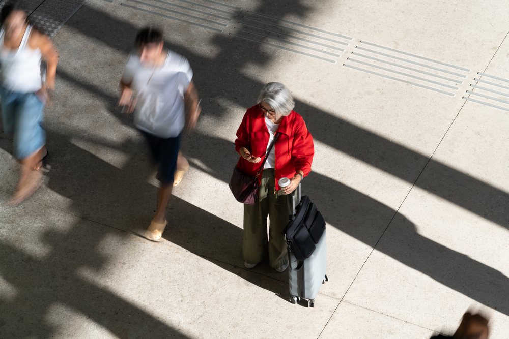Older white woman standing with luggage and coffee