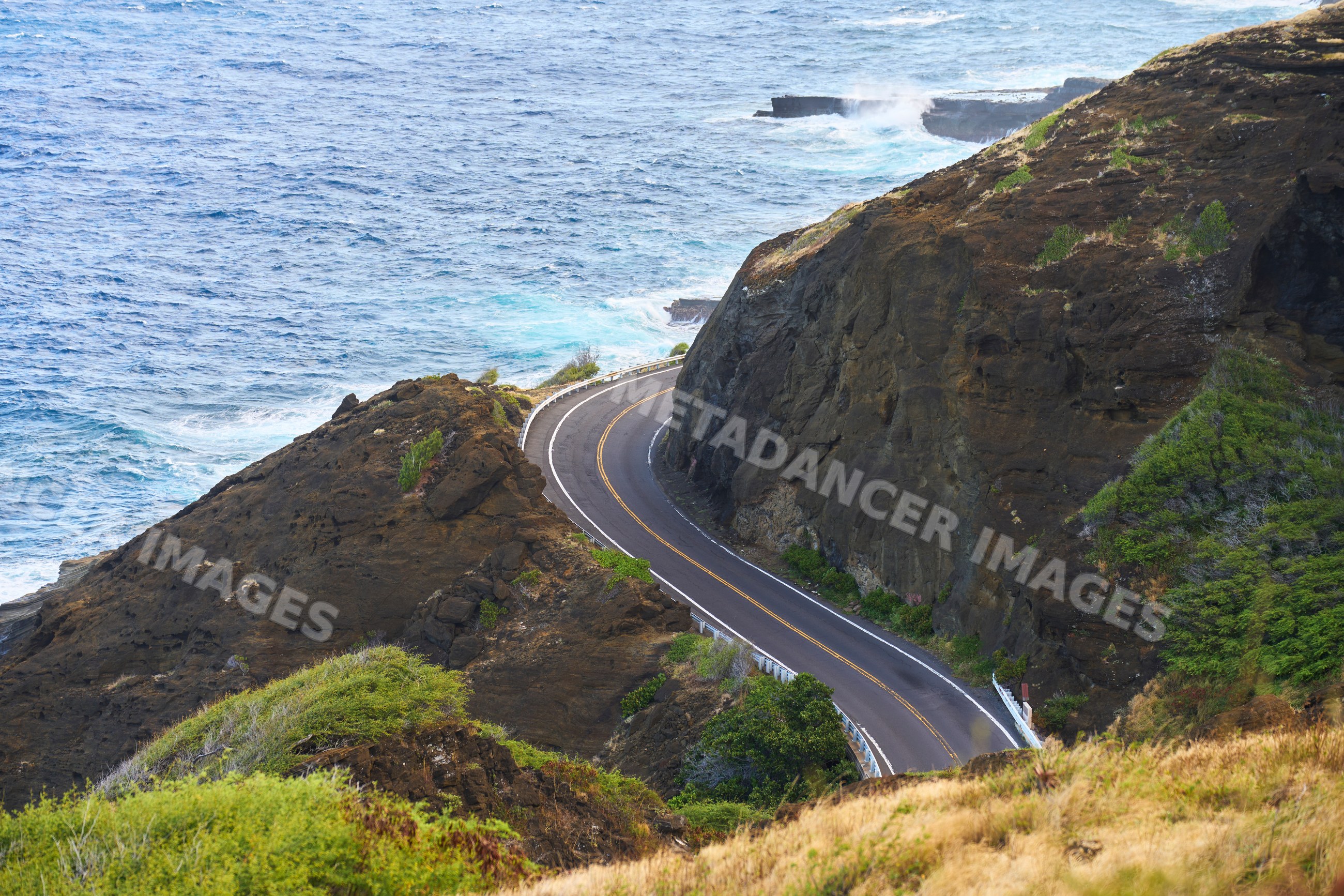 Coastal road curving along cliffs with ocean waves in Oahi, Hawaii