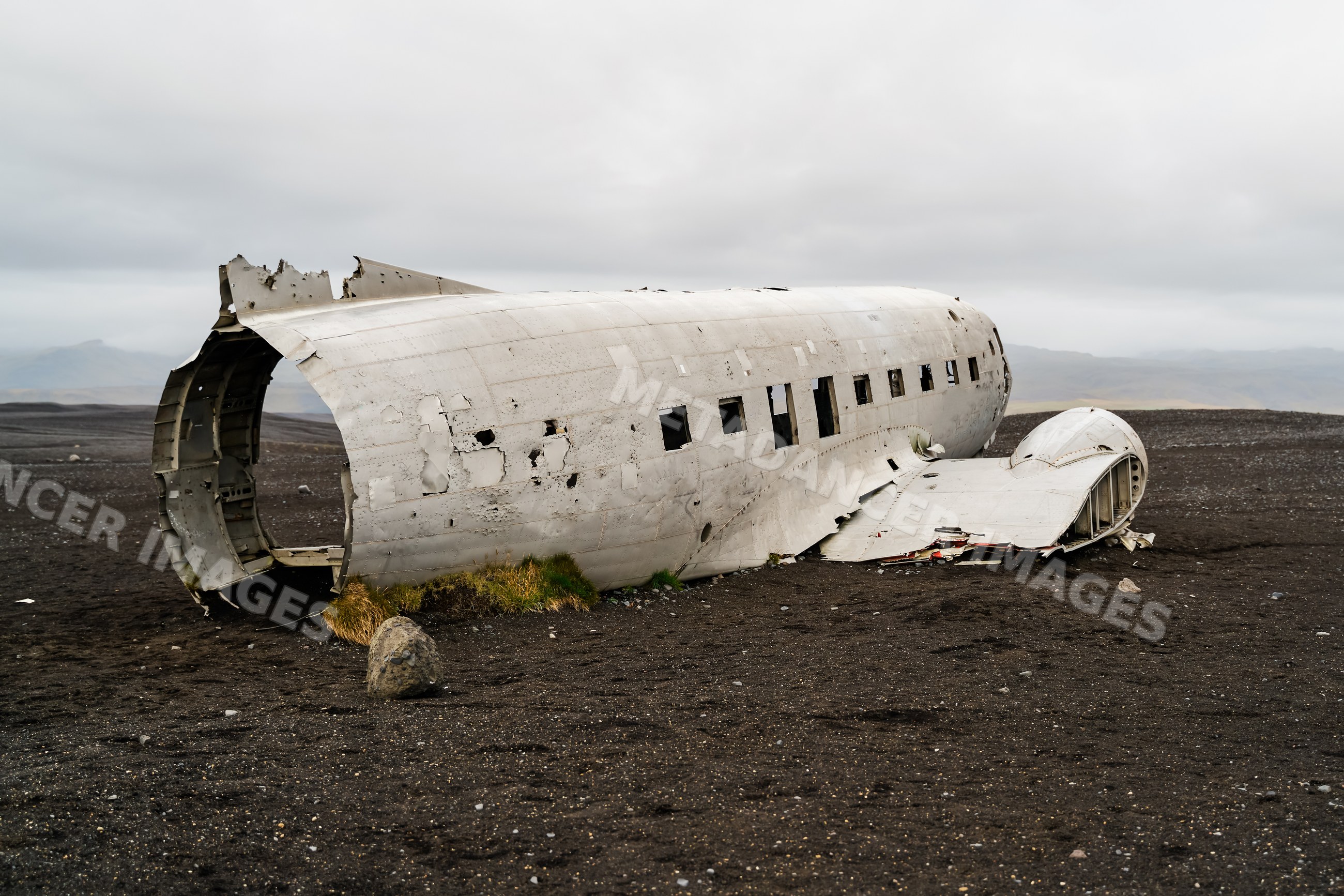 A wrecked airplane fuselage lies abandoned on black sand
