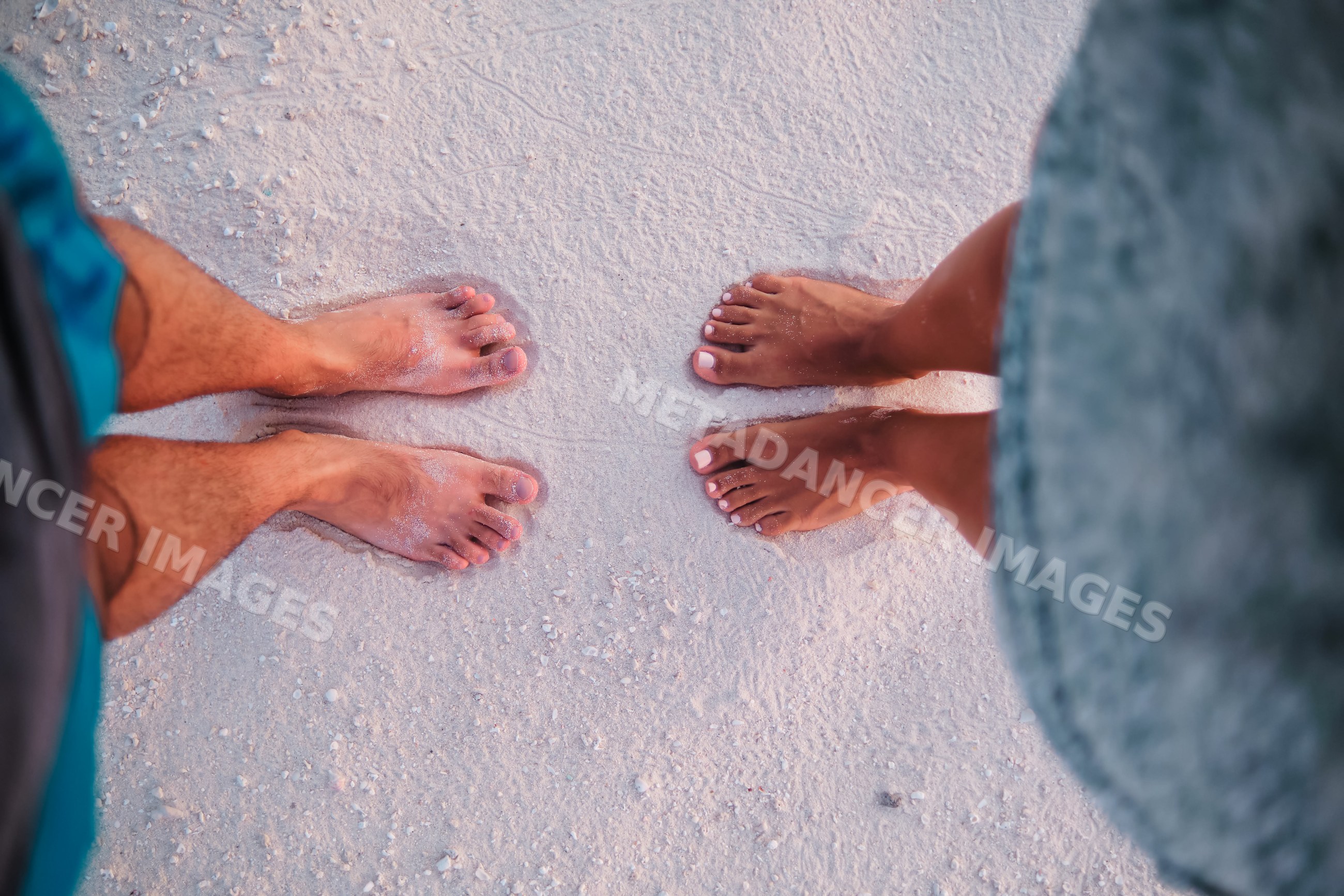 A couple standing barefoot on a sandy beach in a beach