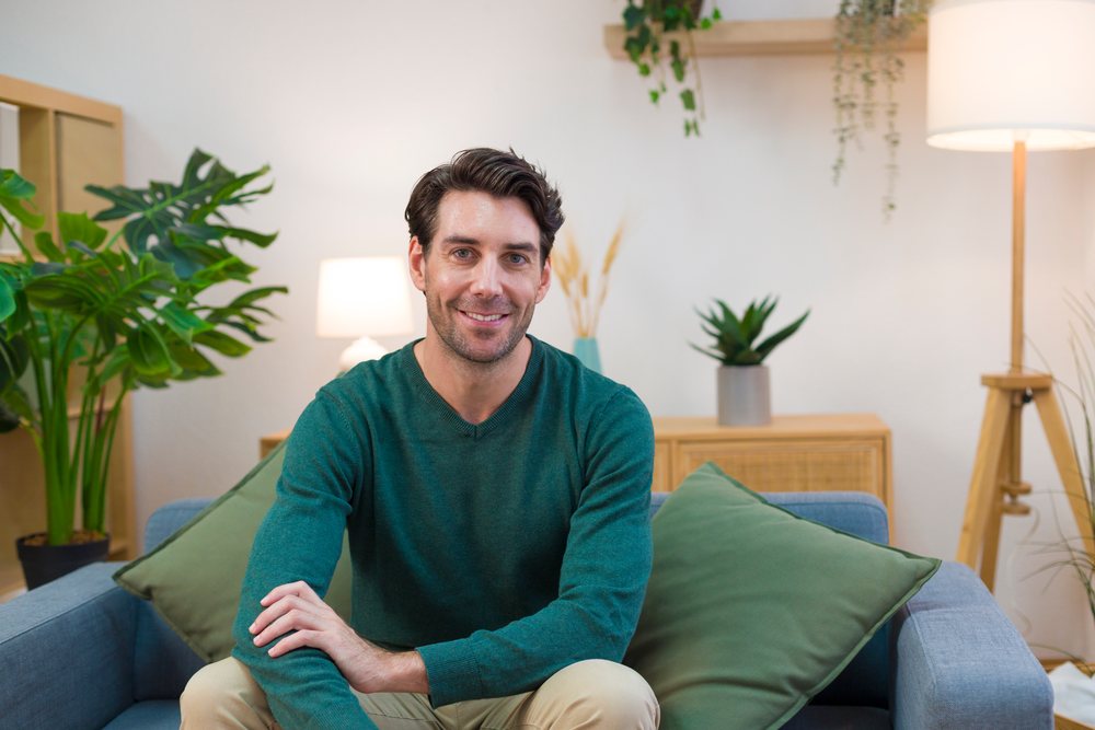 White man sitting on couch smiling in modern living room interior