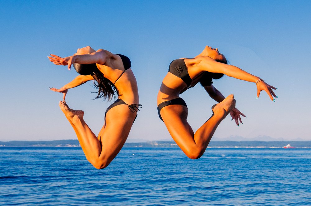 Two women performing partner acrobatics leap over ocean in washington