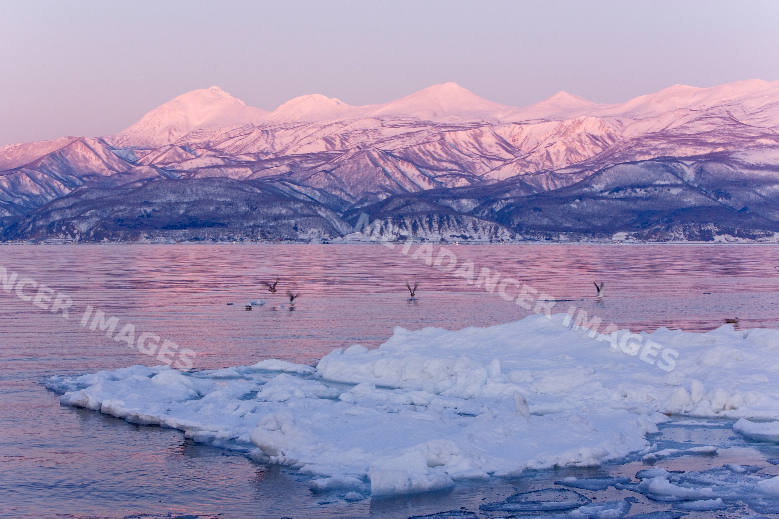 Sun rising over ice floe and snowy mountains japan