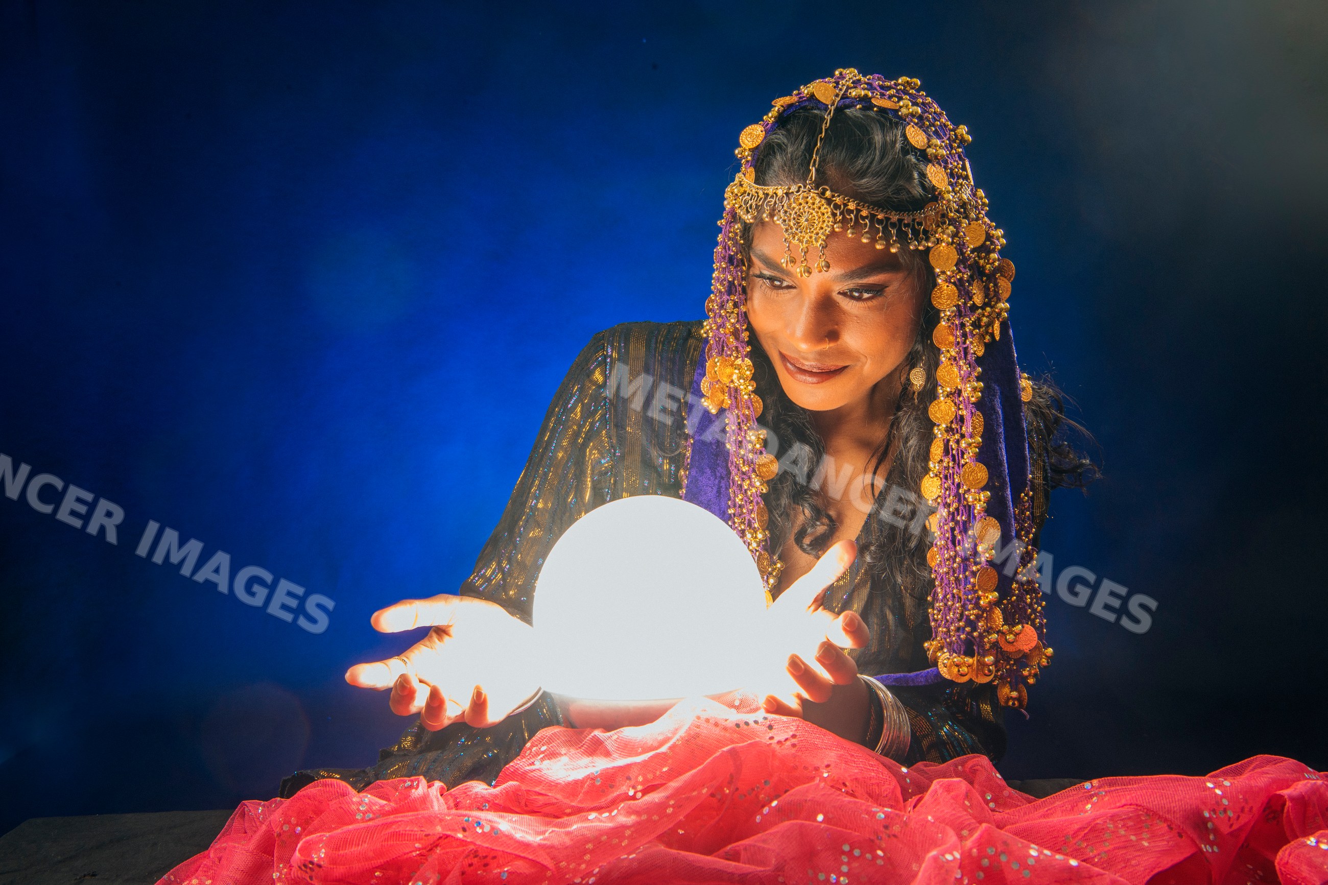 A South Asian woman dressed as a fortune teller gazes into a glowing