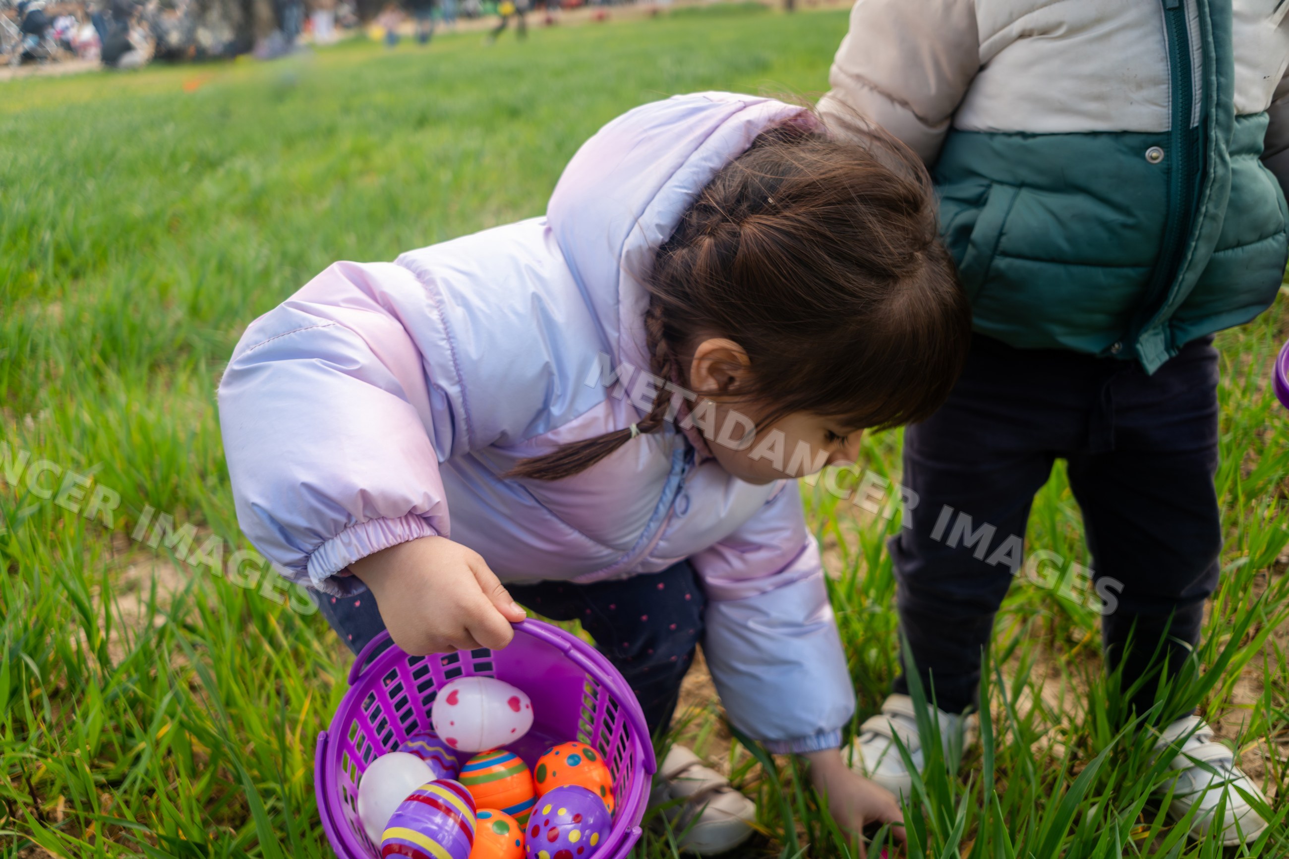 A young white girl collects colorful eggs during an outdoor egg hunt