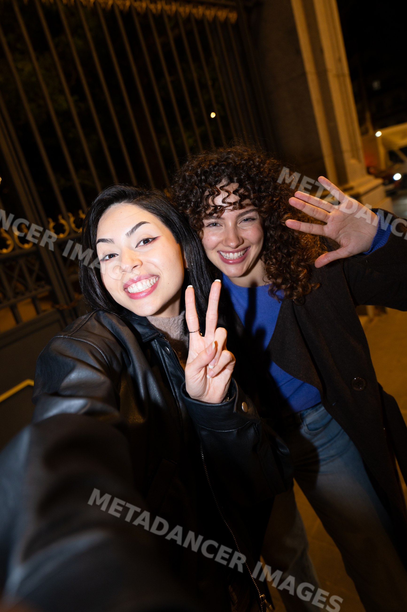 Two Hispanic and white women smiling and waving for a selfie on street