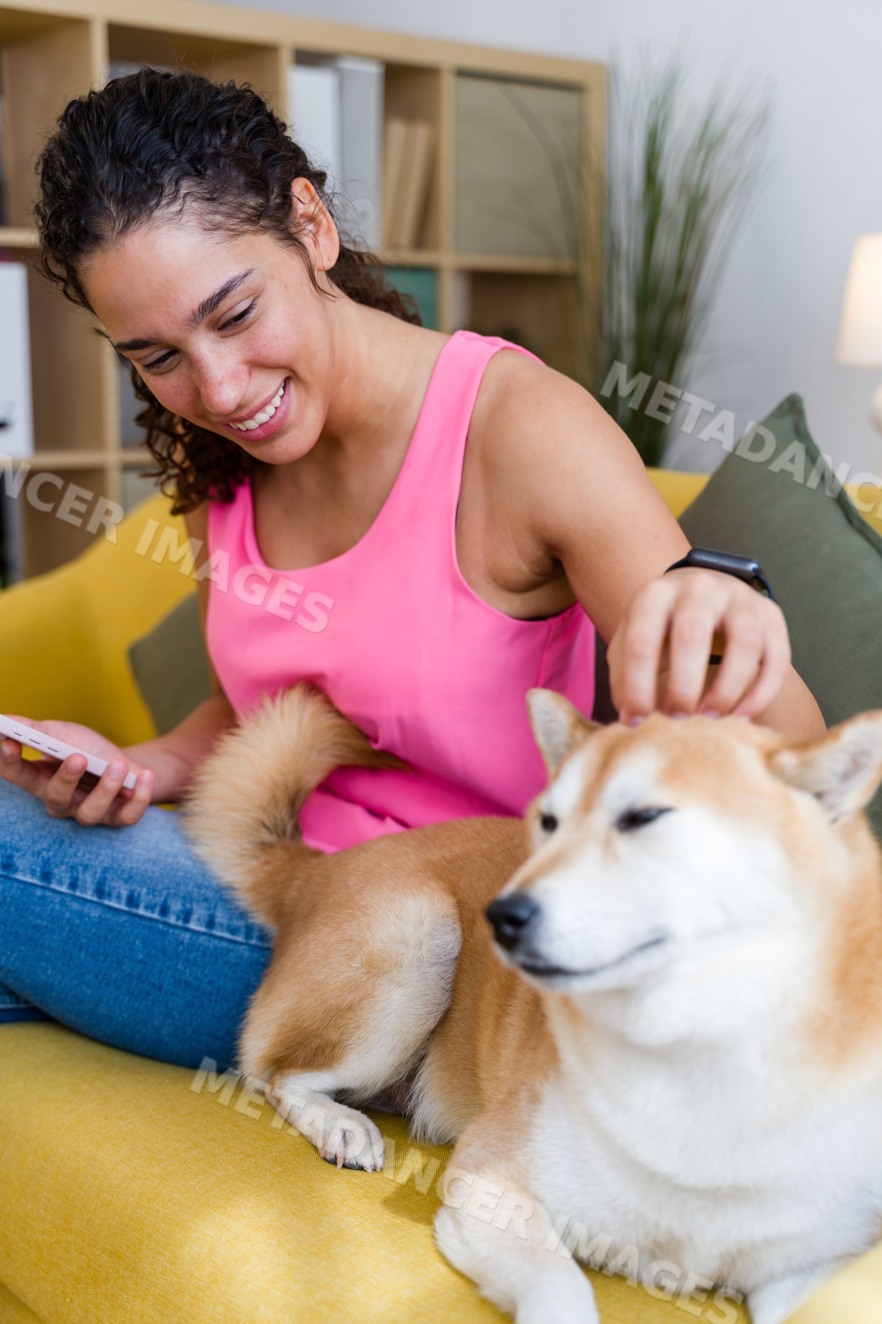 A Hispanic woman smiles while petting her dog on a yellow couch