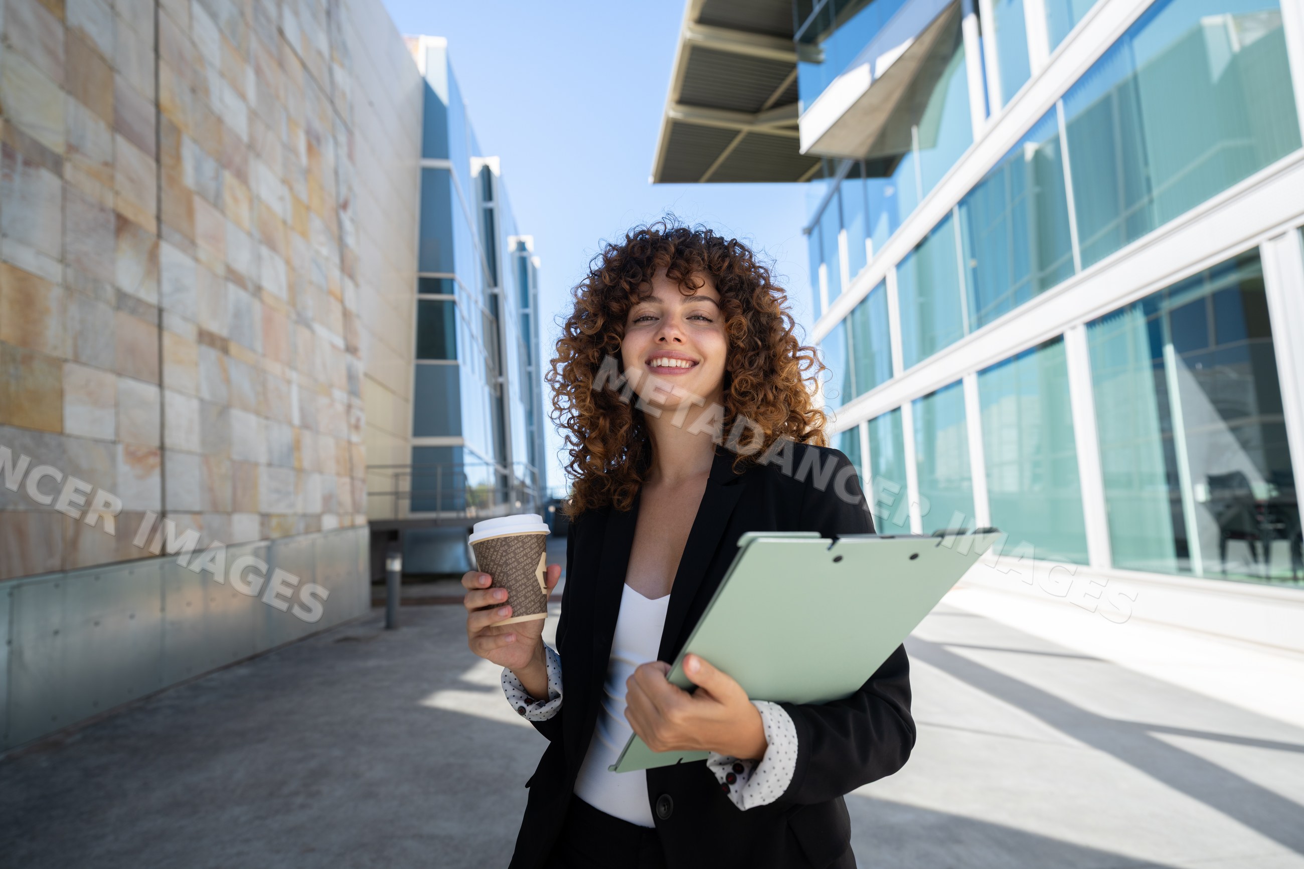Businesswoman holding coffee and clipboard outside modern office
