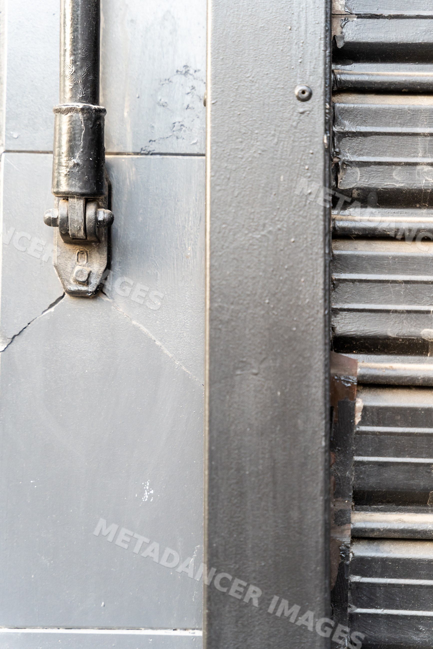 Black metal hinge on gray textured wall with metal shutter