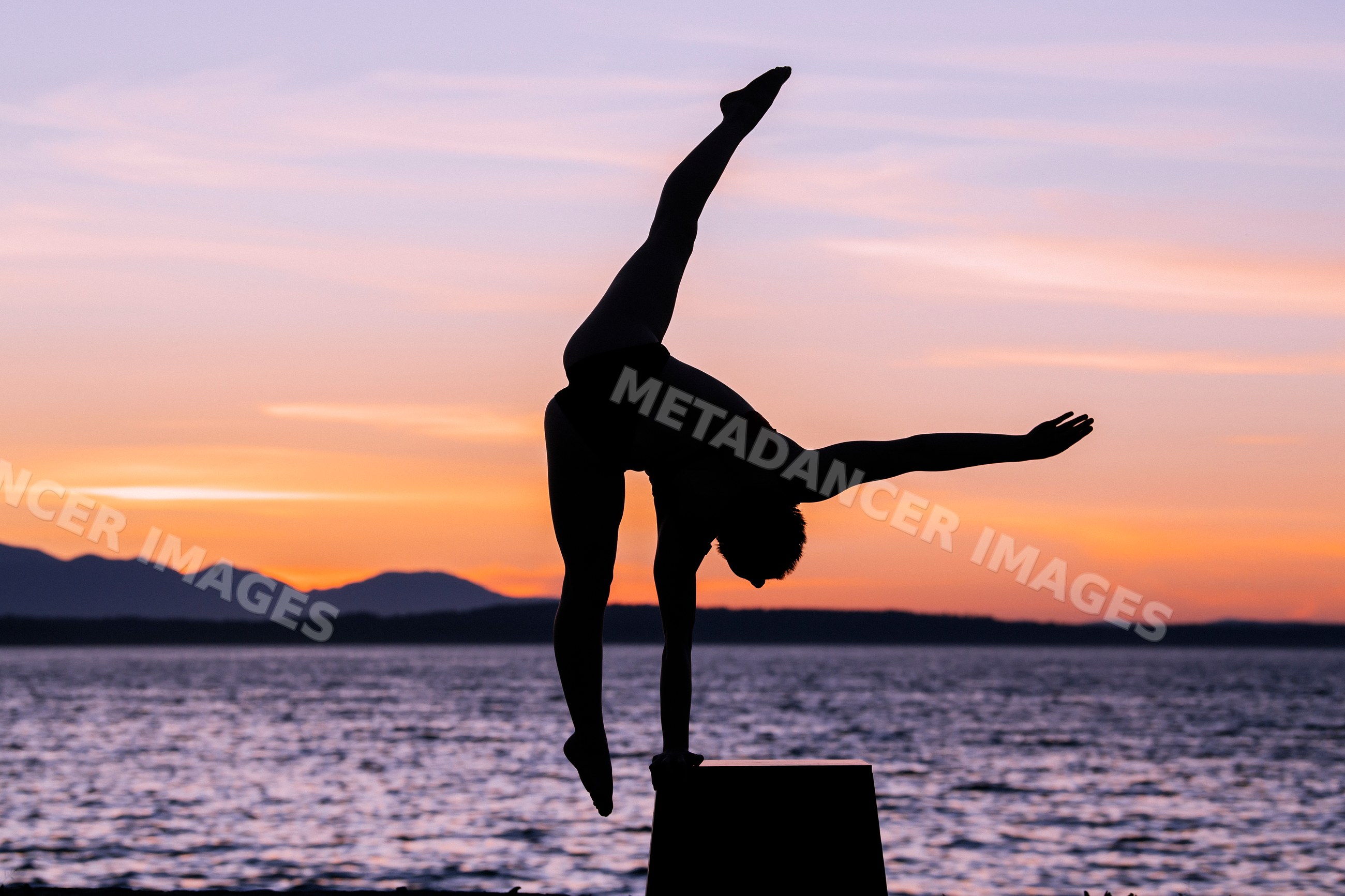 Silhouette of white woman performing handstand by lake at sunset