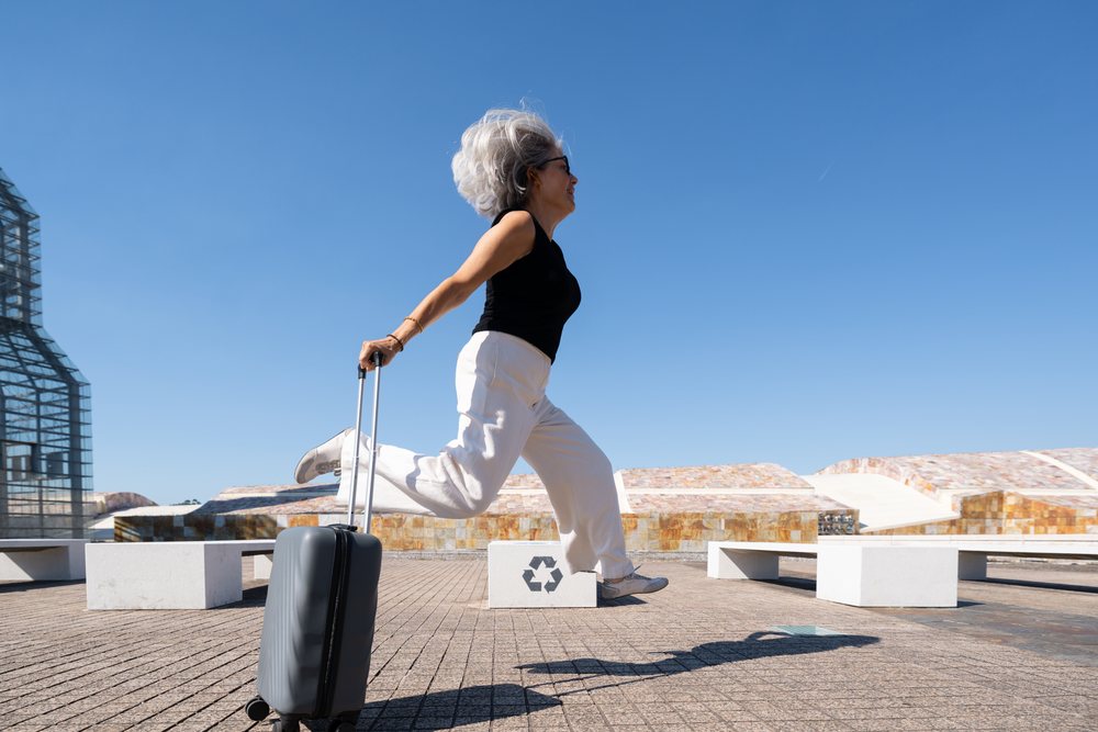 White woman jumping with suitcase outdoors in urban Spain