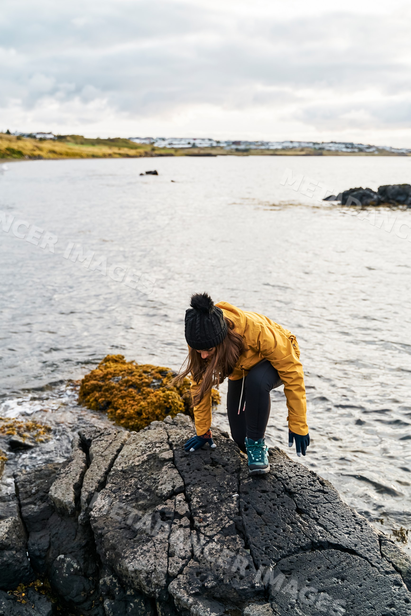 A white woman climbs volcanic rocks along a rocky shore