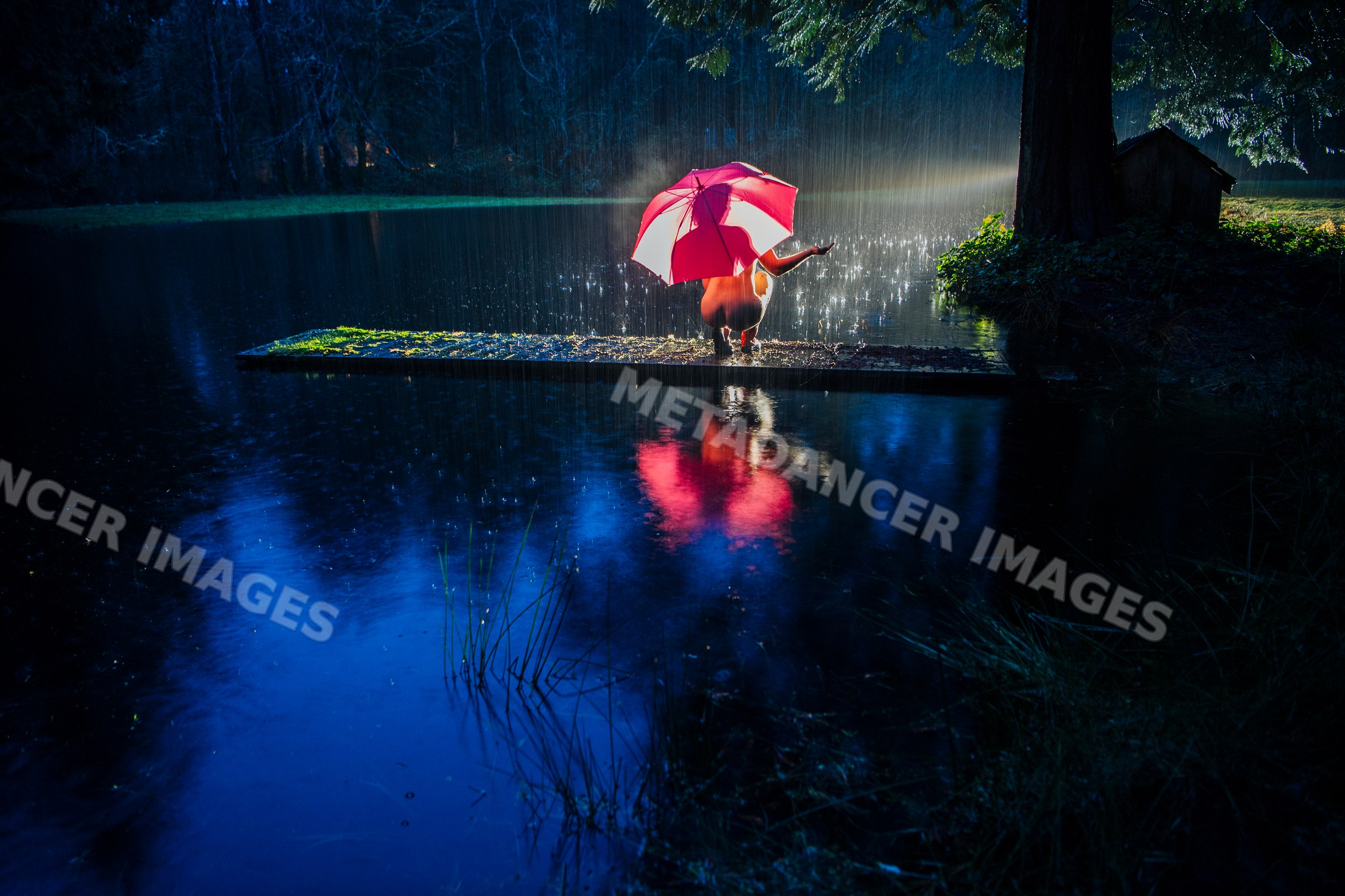 White woman with red umbrella sitting on dock in rain at night