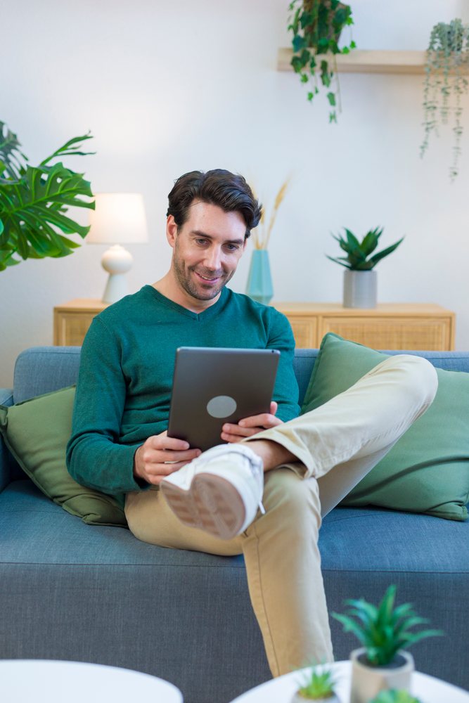 White man sitting on sofa using tablet in modern living room