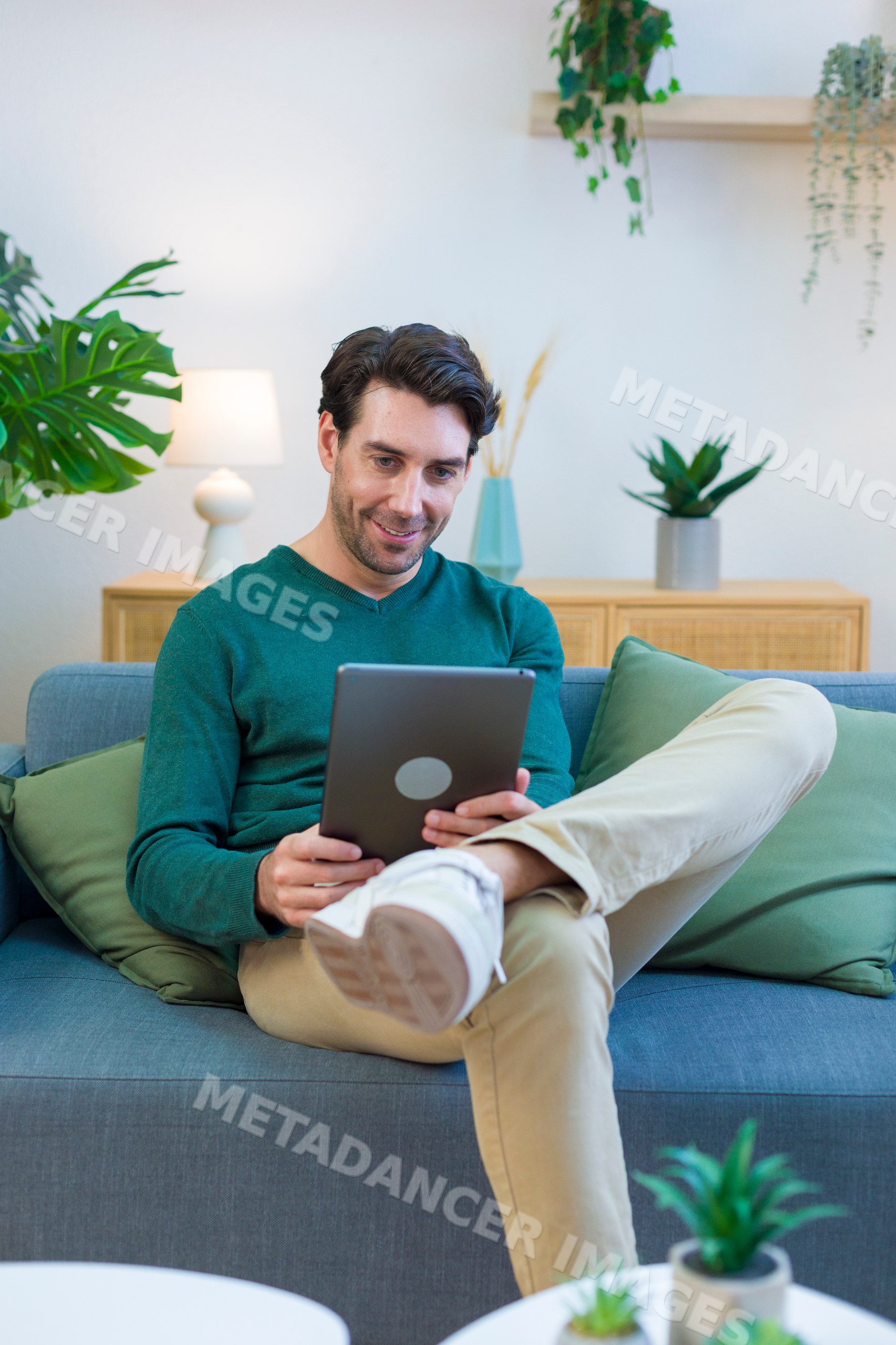 White man sitting on sofa using tablet in modern living room