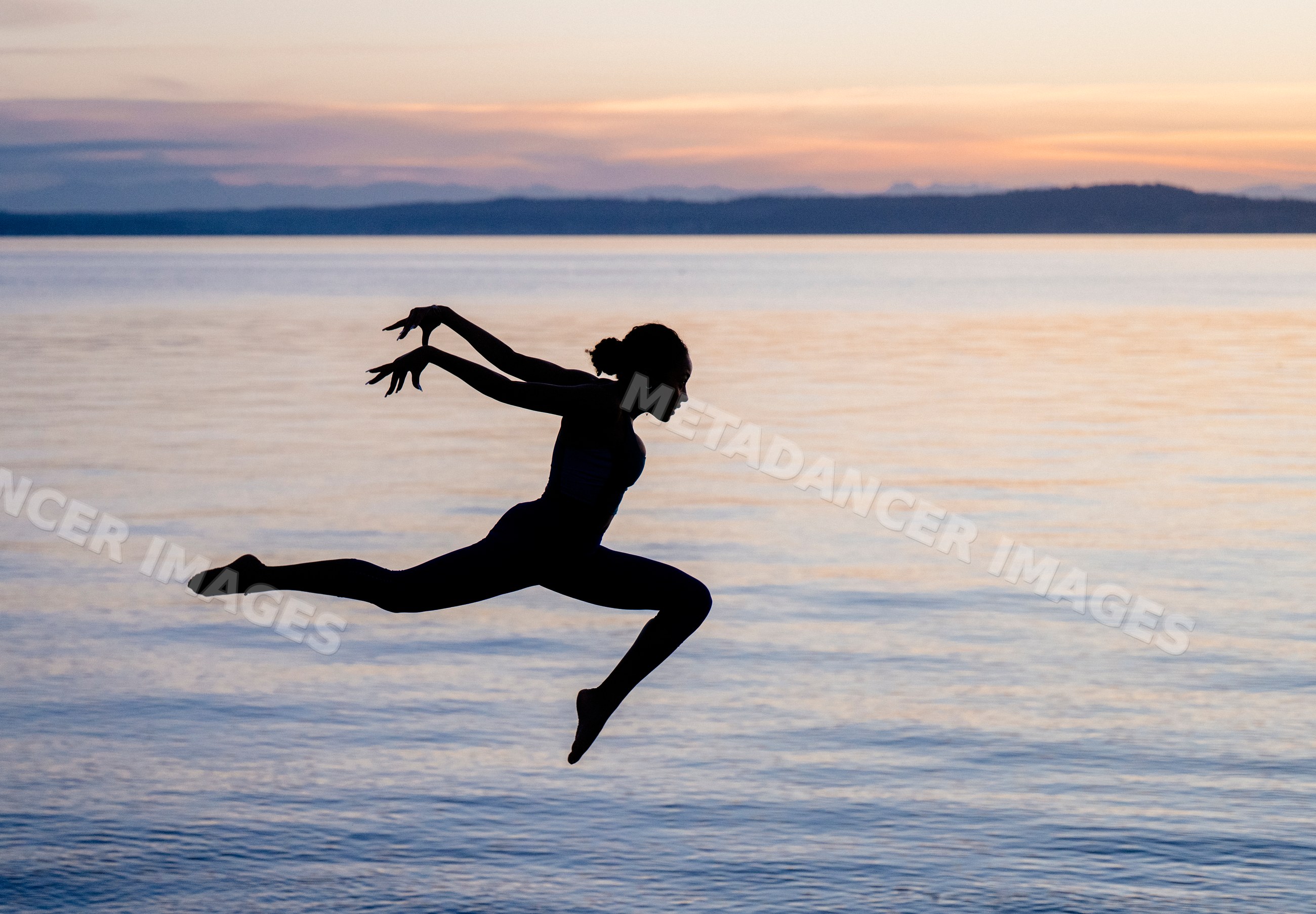 Hispanic woman performing yoga jump silhouette at lake during sunset