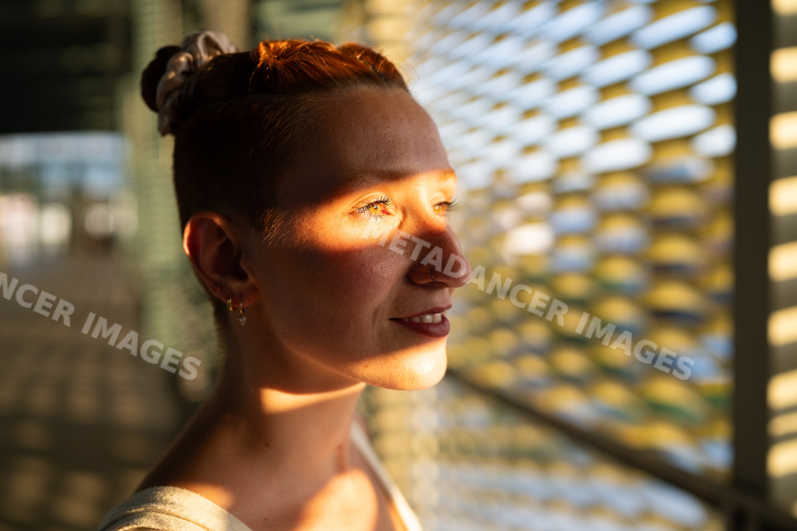 A woman smiles with sunlight creating shadows on her face indoors