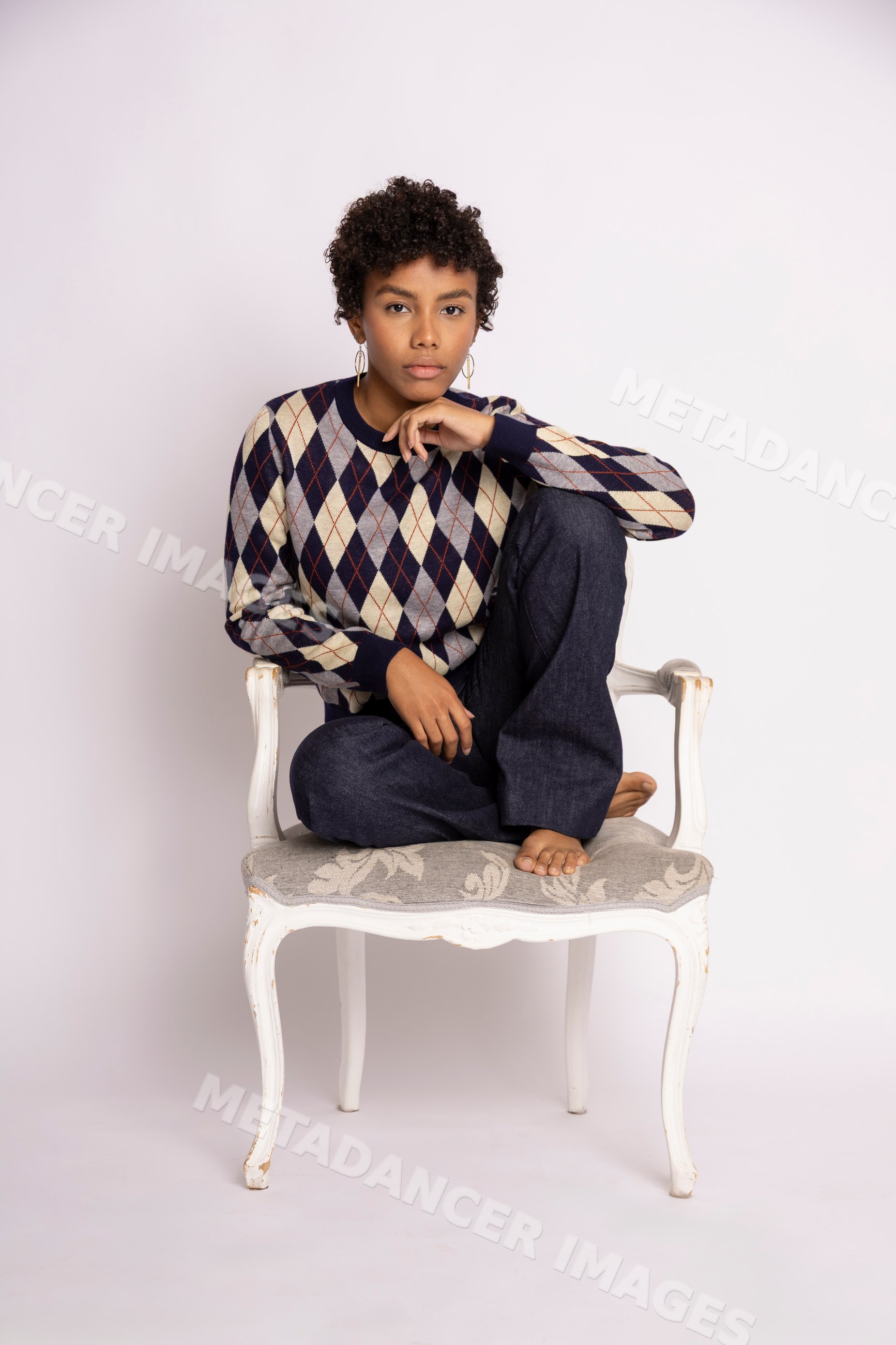 Hispanic woman sitting on white chair wearing argyle patterned sweater