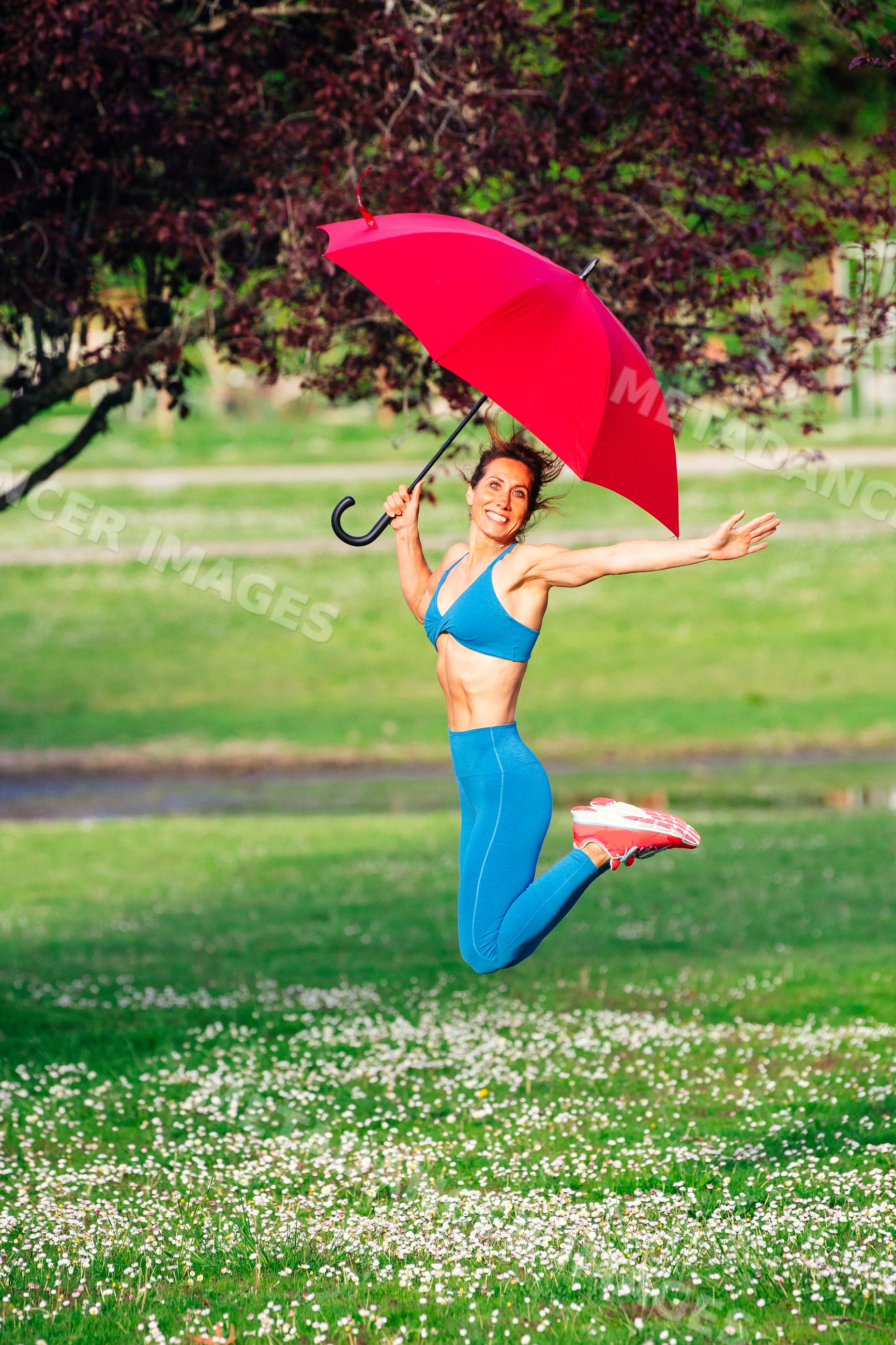 White woman jumping with red umbrella on grassy field