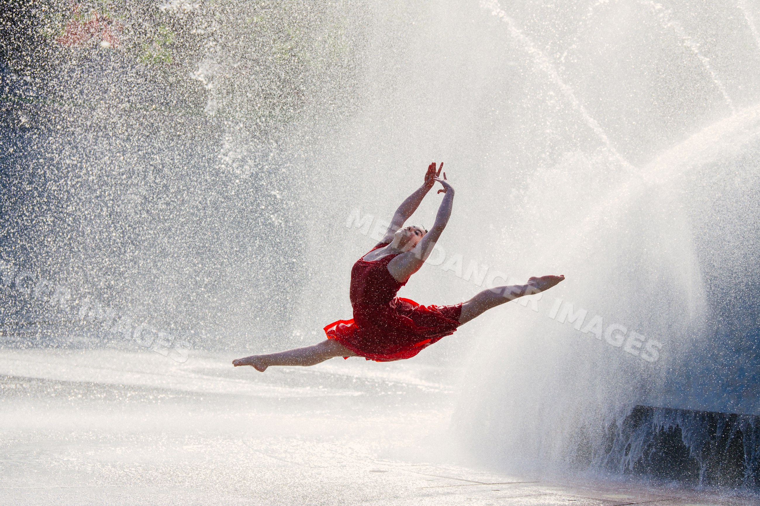 White dancer leaping through water spray from outdoor fountain