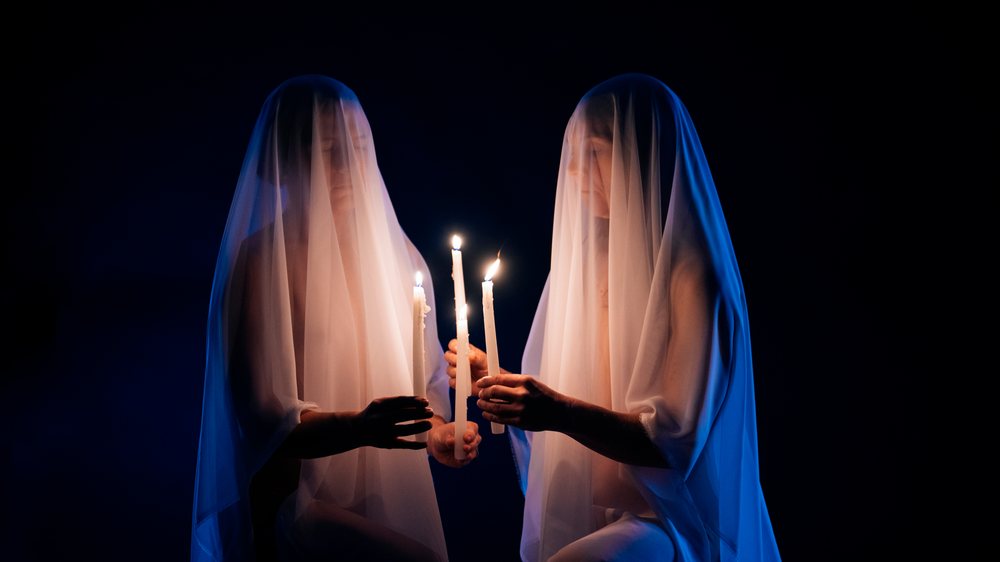 Two ghostly veiled figures holding lit candles in dark setting