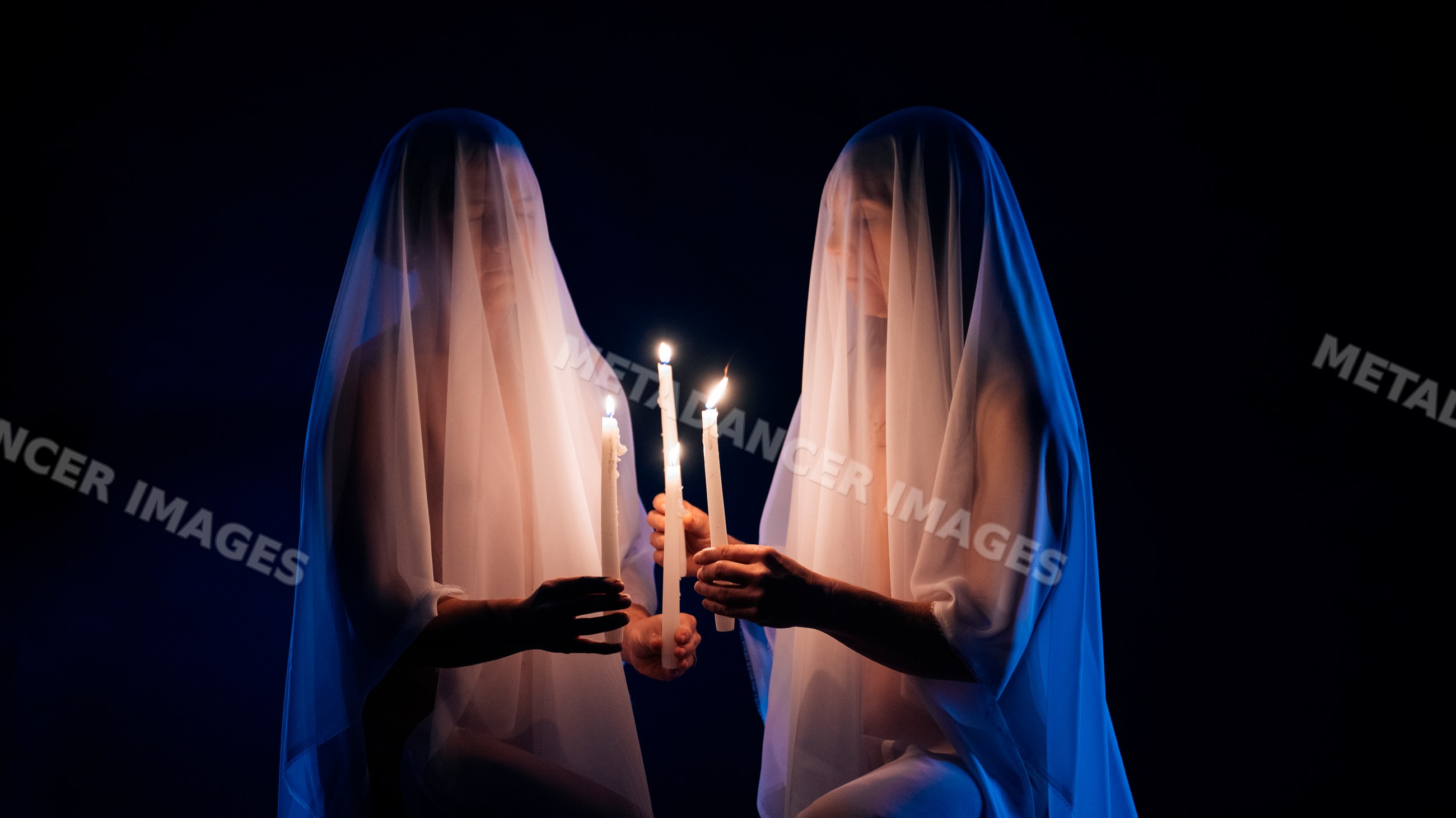 Two ghostly veiled figures holding lit candles in dark setting