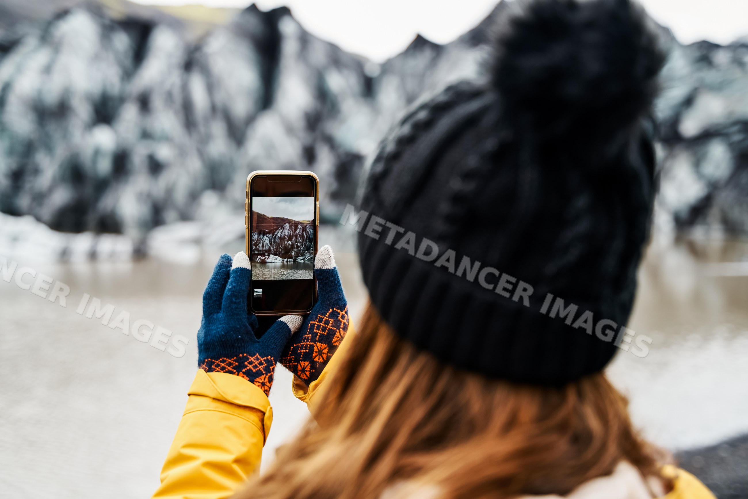 A white person photographs a glacier mountain landscape over a lake