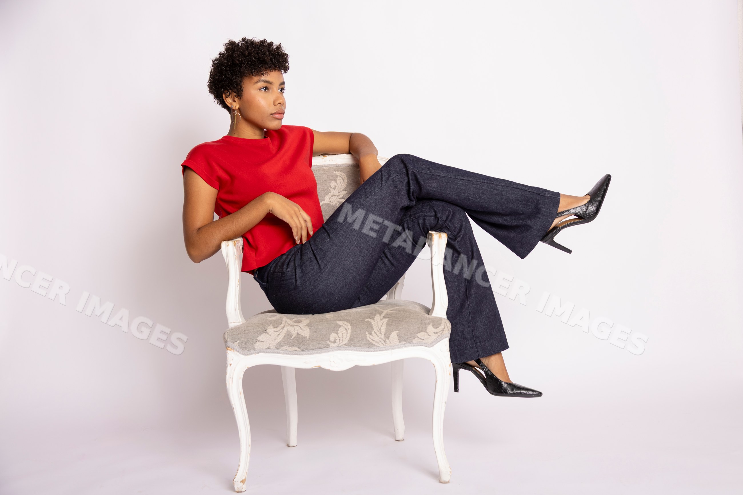 Hispanic woman in red top and blue jeans posing seated on decorative